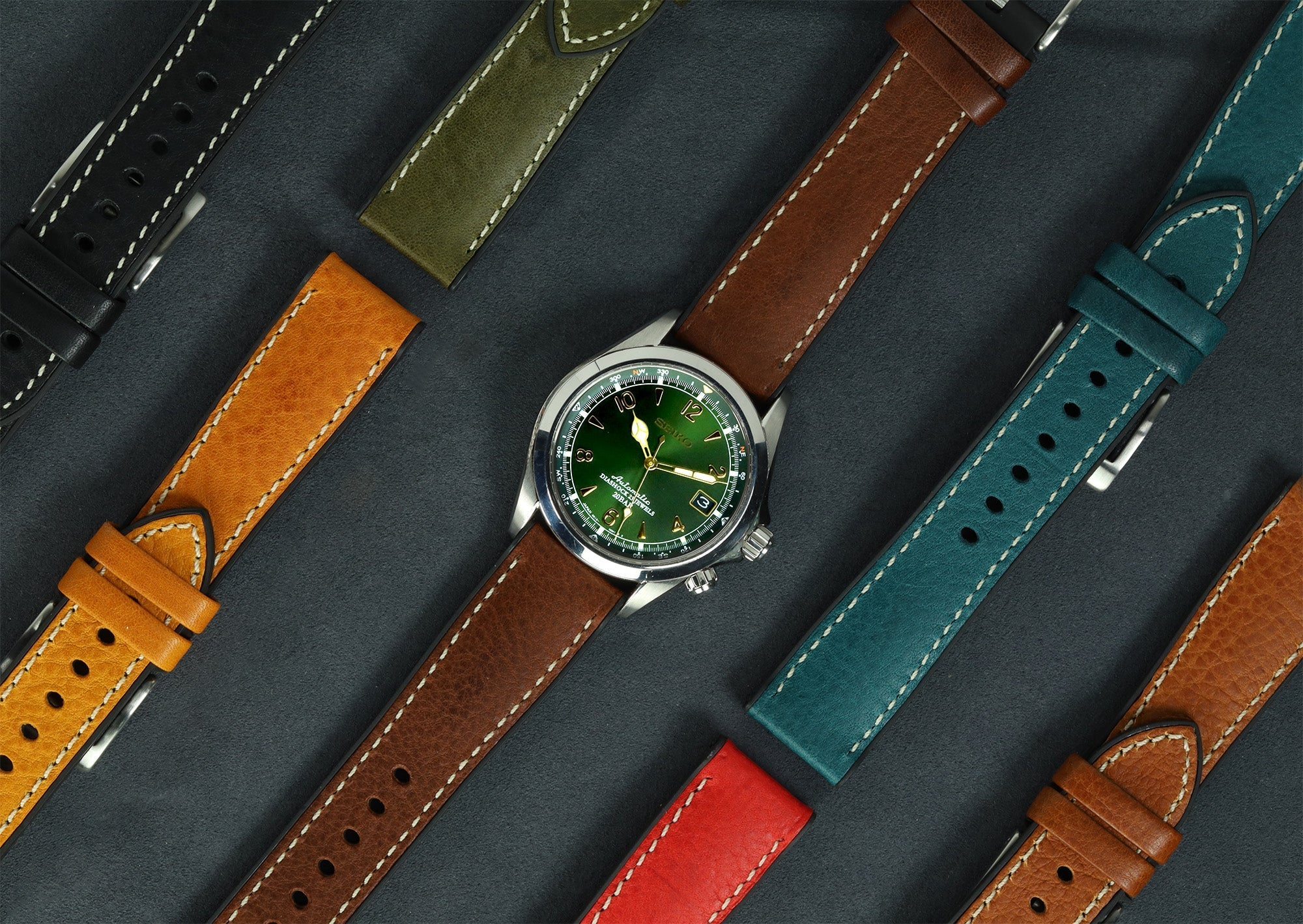 Stainless steel watch with green dial and brown leather strap surrounded by interchangeable colorful leather and rubber watch bands