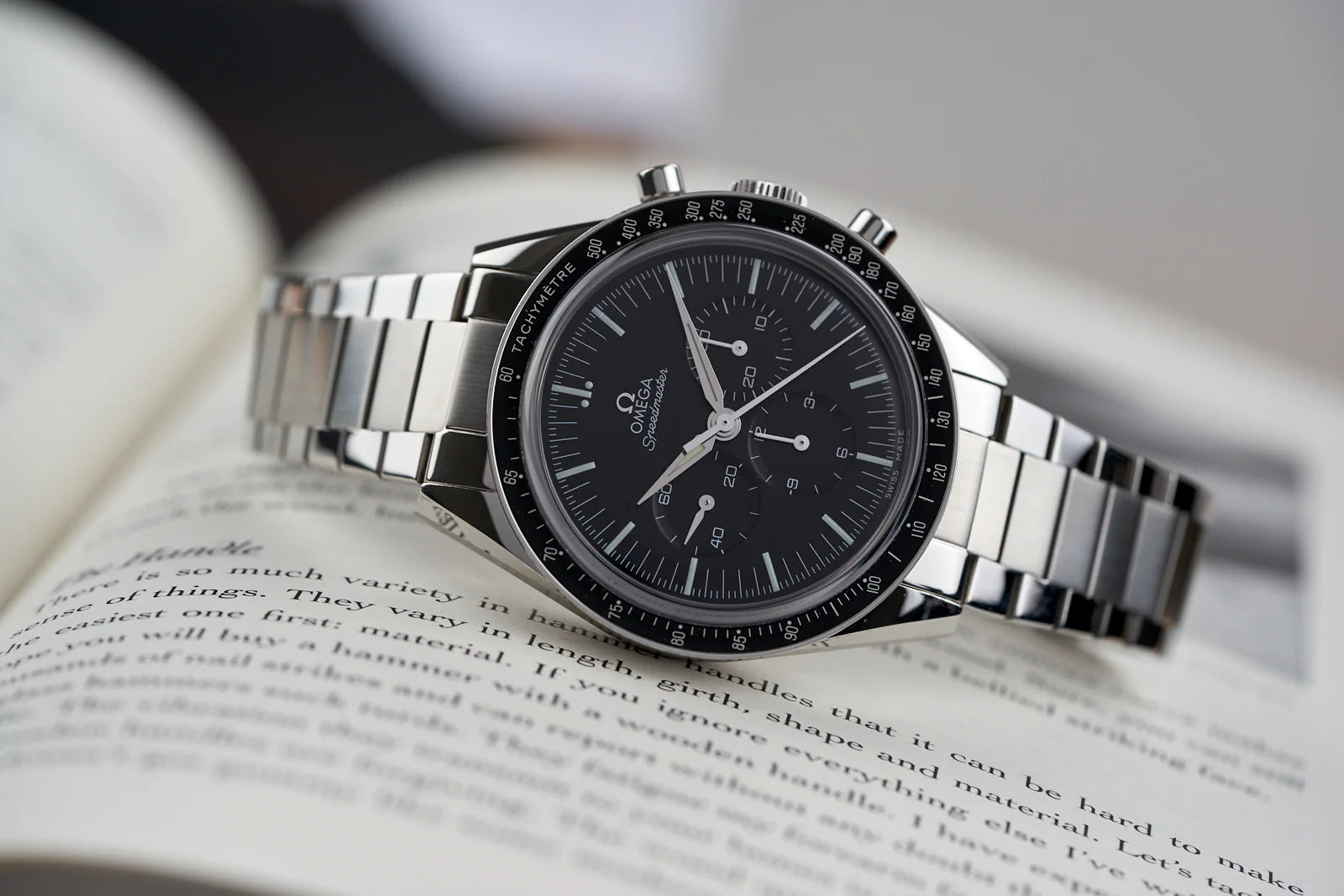 Omega Speedmaster chronograph watch with black dial and tachymeter bezel on stainless steel bracelet resting on open book