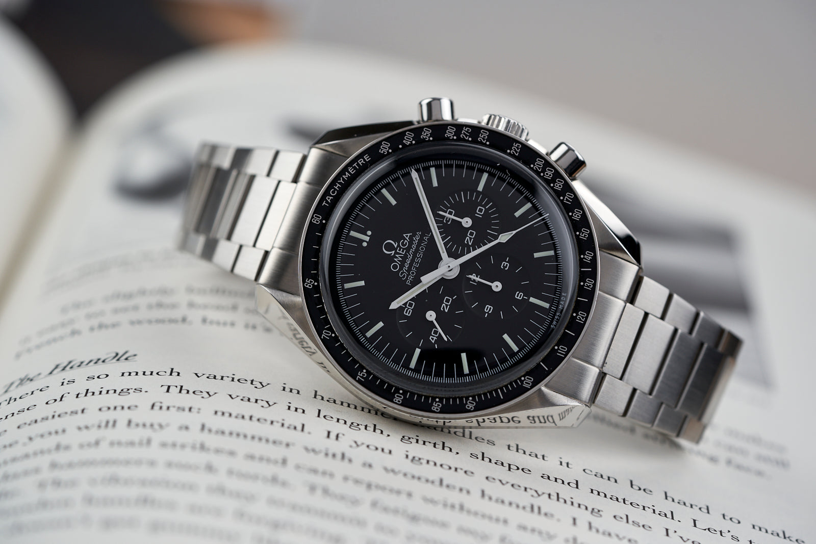 Omega Speedmaster chronograph watch with black dial and stainless steel flat link bracelet on open book page