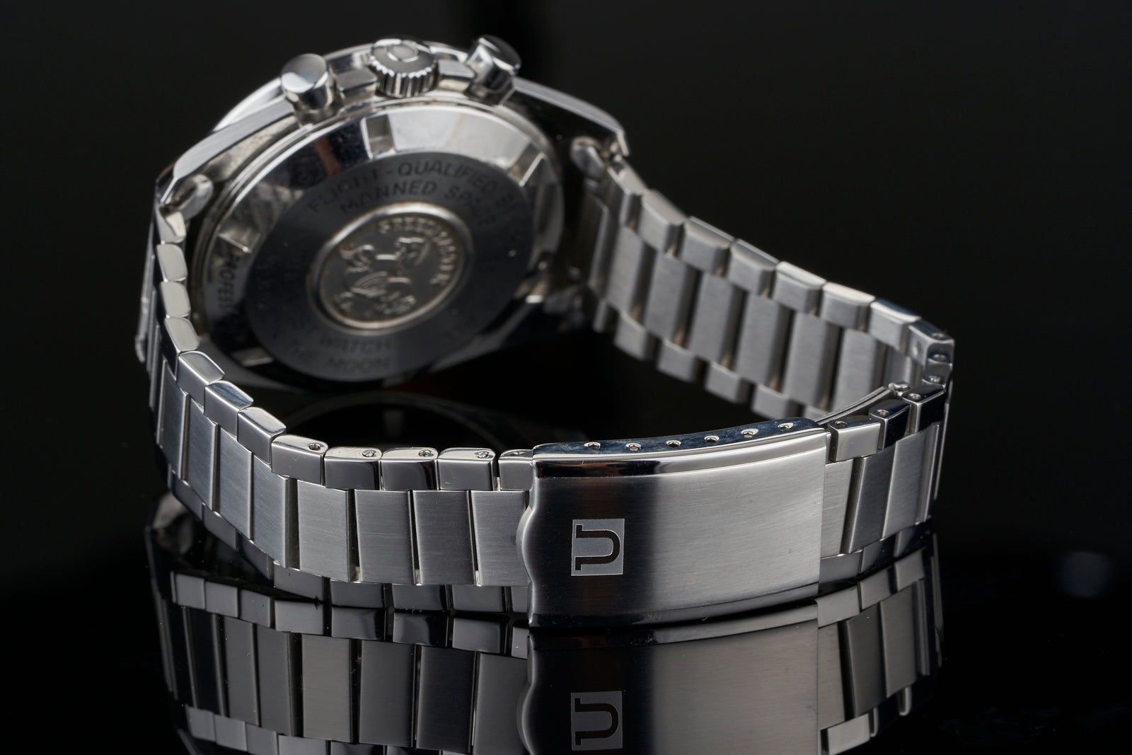 Stainless steel chronograph watch with flat link metal bracelet and embossed caseback, displayed against black background