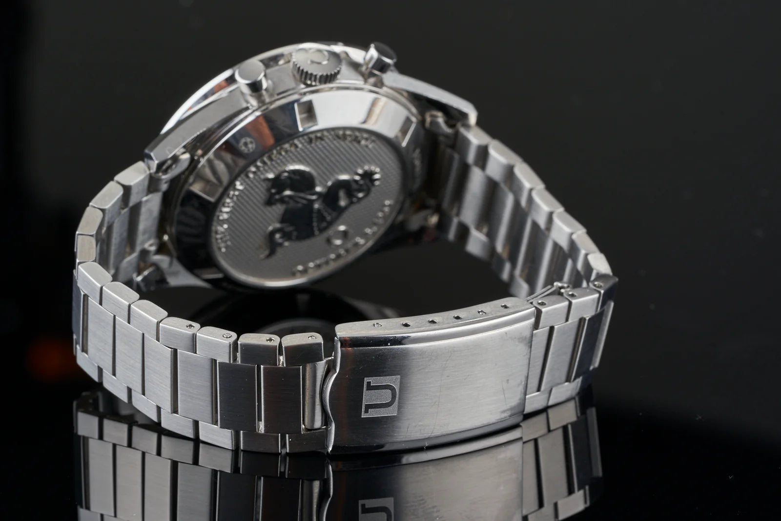 Stainless steel chronograph watch with flat link bracelet and dark dial, displayed at angle against black background