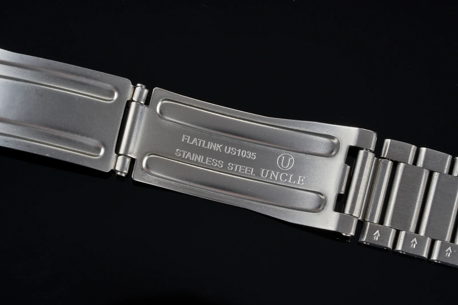 Stainless steel flat link watch bracelet with signed clasp and Uncle branding on black background