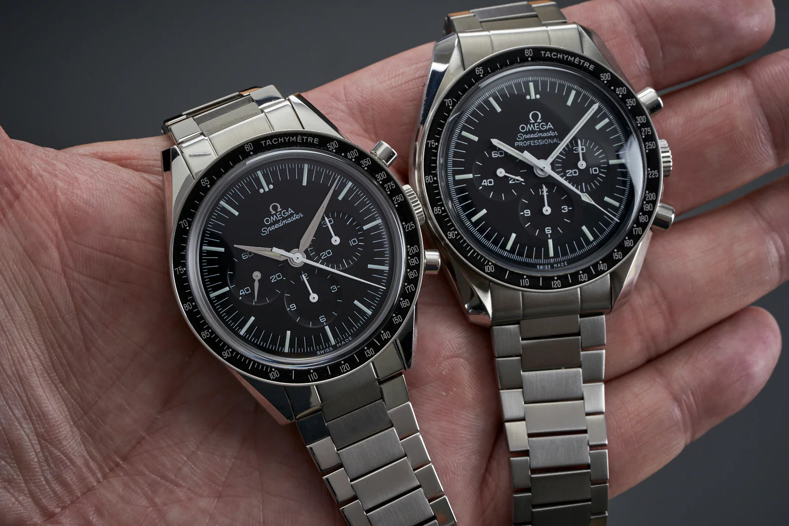 Two Omega Speedmaster Professional chronograph watches with stainless steel bracelets and black dials featuring tachymeter bezels held in hand
