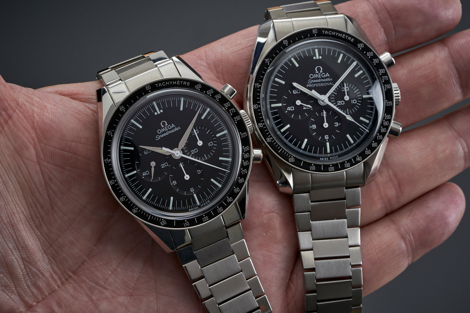 Two Omega Speedmaster professional chronograph watches with black dials and tachymetre bezels on stainless steel bracelets held in hand