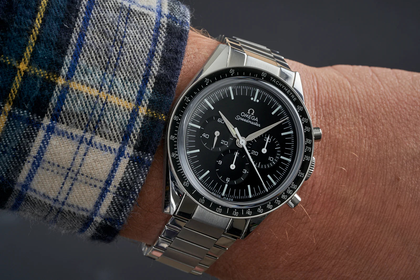 Omega Speedmaster chronograph watch with stainless steel flat link bracelet on wrist, black dial with tachymetre bezel