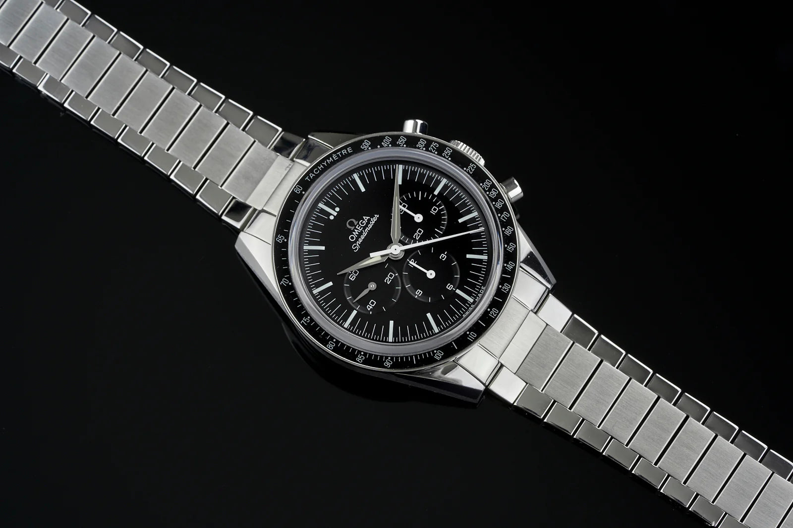 Omega Speedmaster chronograph watch with black dial, tachymeter bezel, and stainless steel flat link bracelet on black background