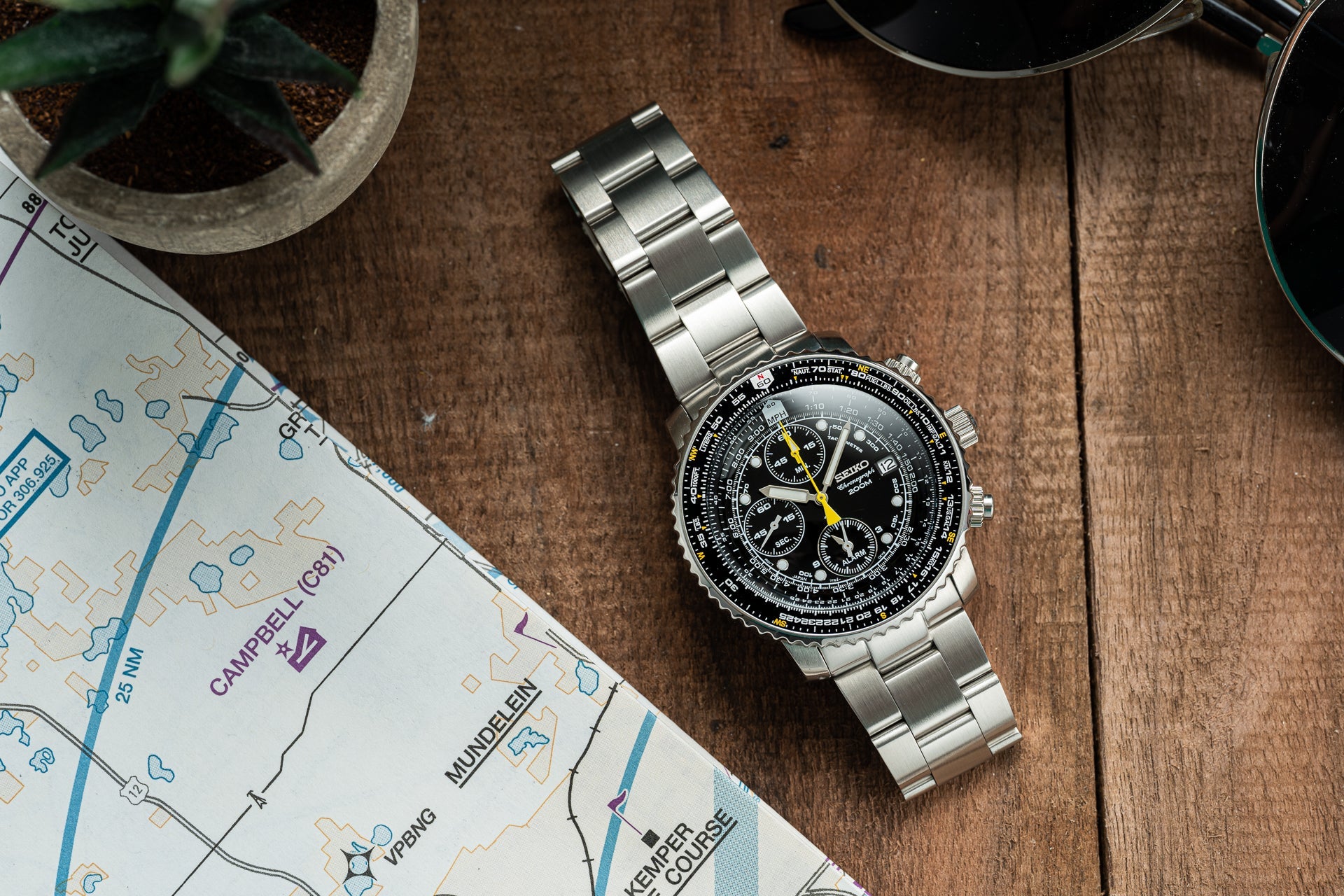 Silver stainless steel Seiko SNA411 Flightmaster chronograph watch with black dial and yellow accents on wooden surface next to map