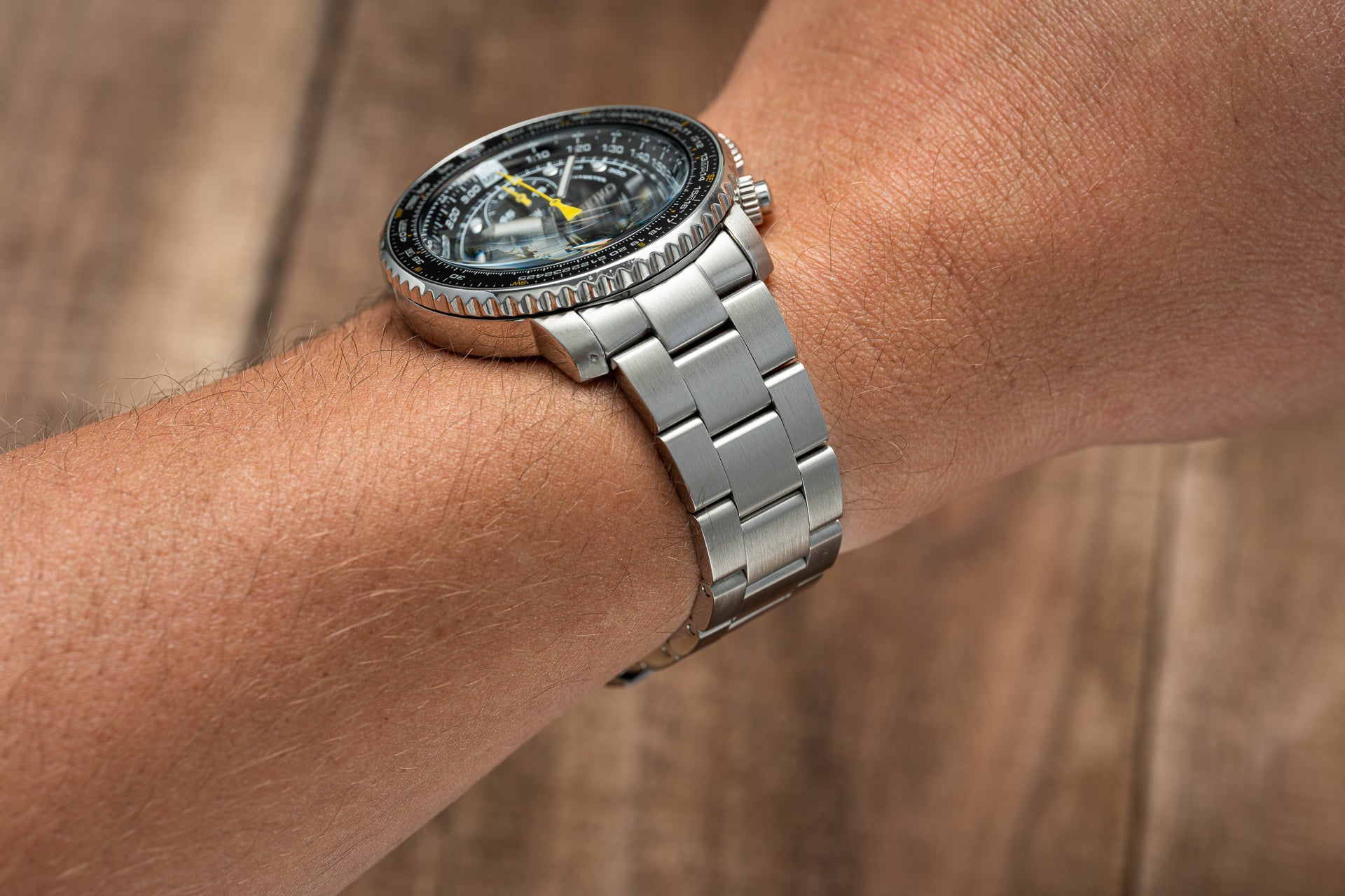 Silver stainless steel chronograph pilot watch with black dial and yellow hands worn on wrist