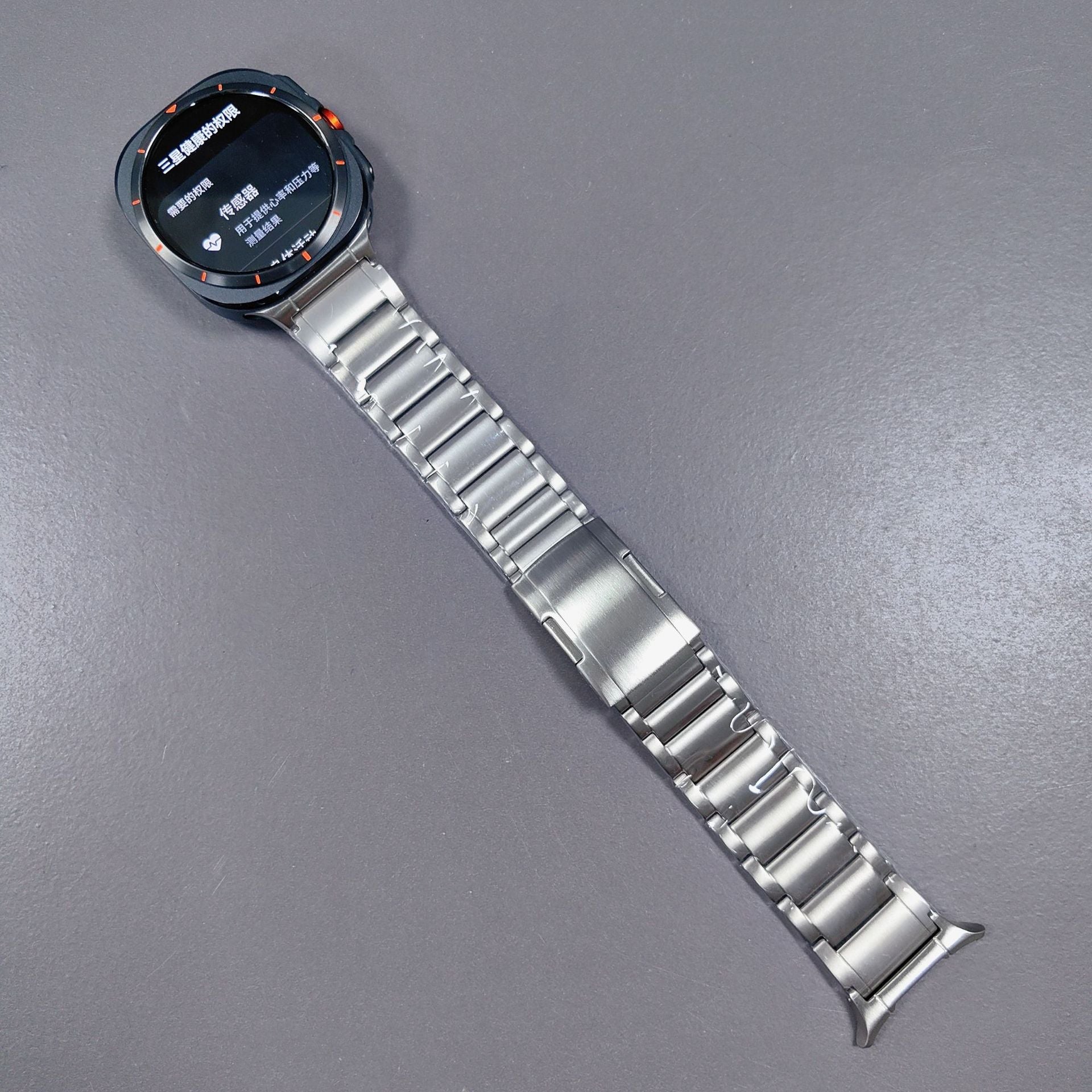 Galaxy Watch Ultra with titanium bracelet band displaying AMOLED screen on gray background