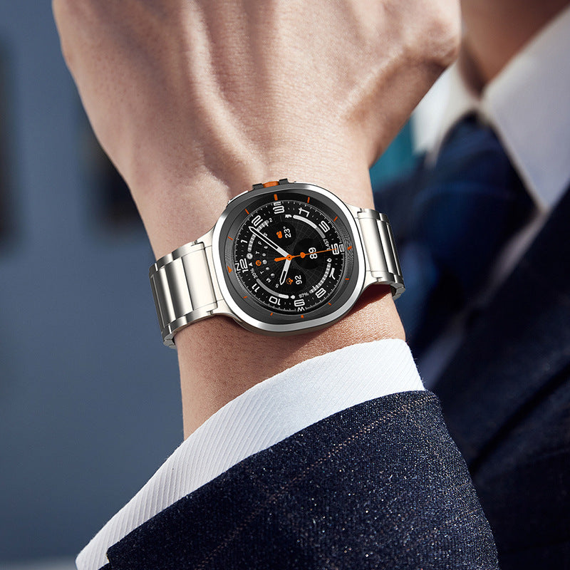 Titanium luxury smartwatch with black dial and orange accents on stainless steel bracelet, worn on wrist with business attire