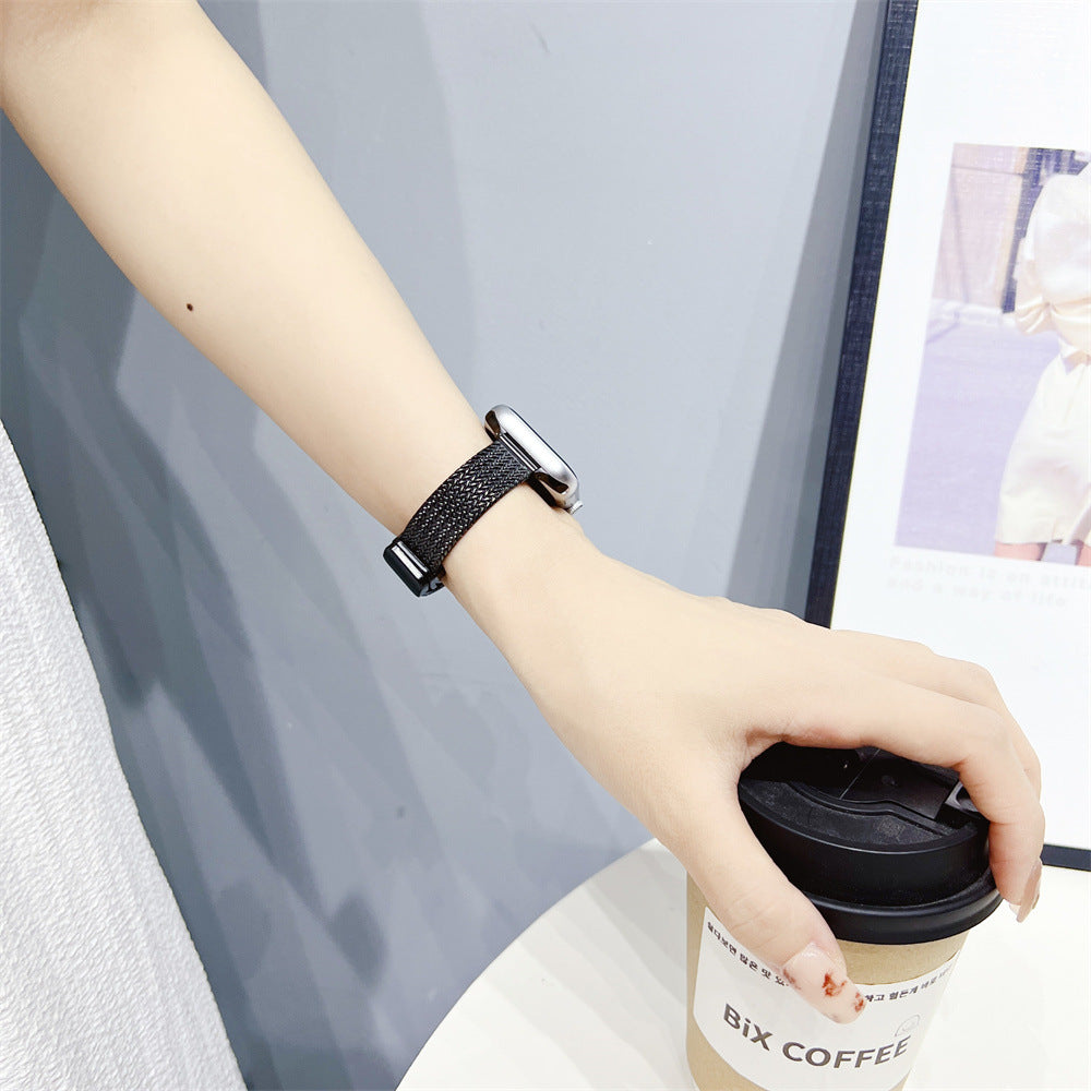 Black herringbone mesh Apple Watch band with polished silver connector worn on wrist holding coffee cup