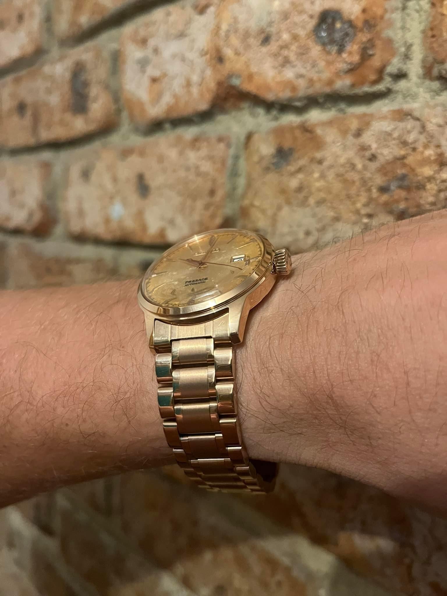 Rose gold curved steel bracelet watch on wrist with champagne dial against brick background