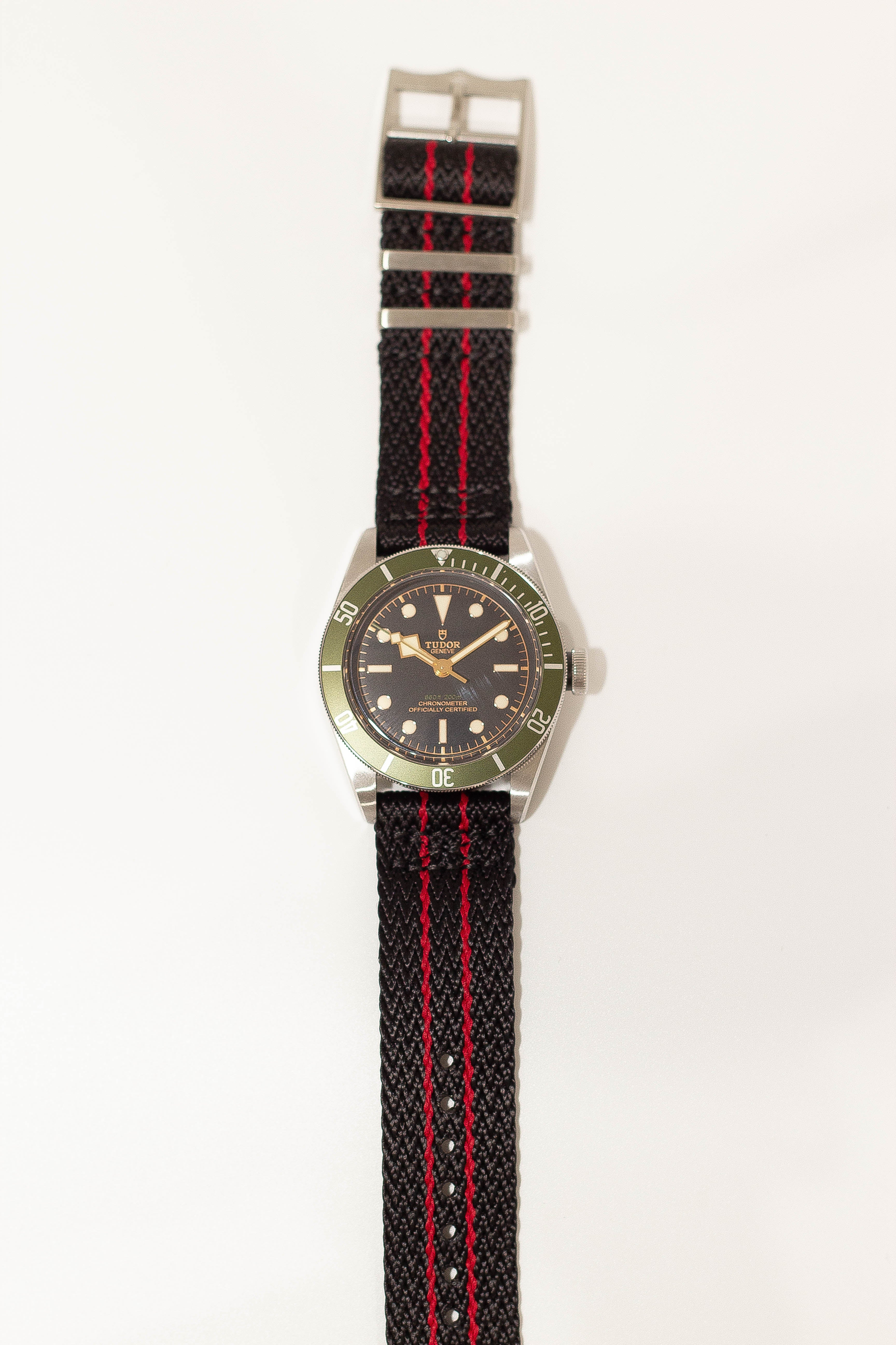 Tudor Black Bay dive watch with green bezel, stainless steel case, and black fabric strap with red stripe