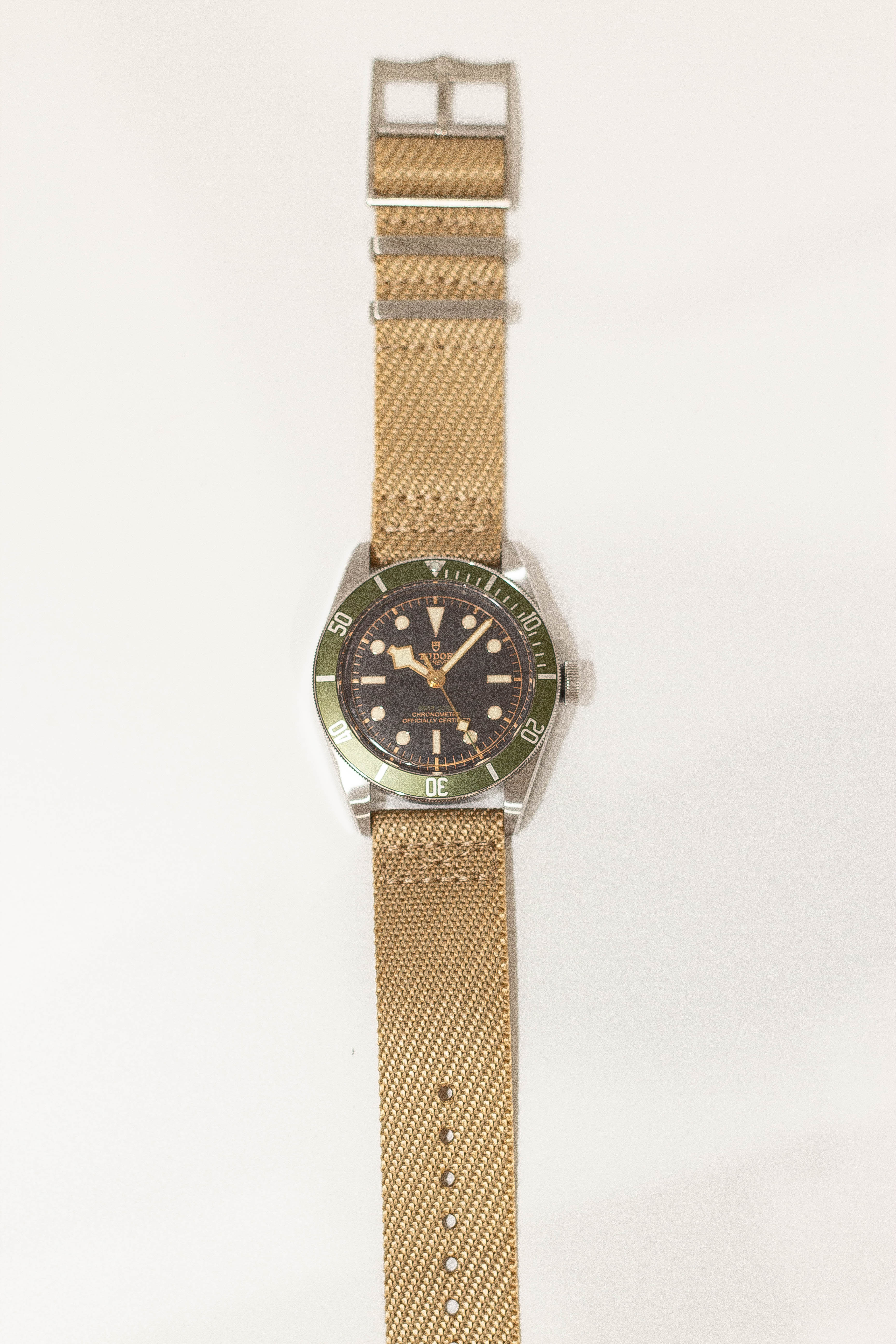 Vintage dive watch with stainless steel case, green bezel, black dial, and tan canvas fabric strap