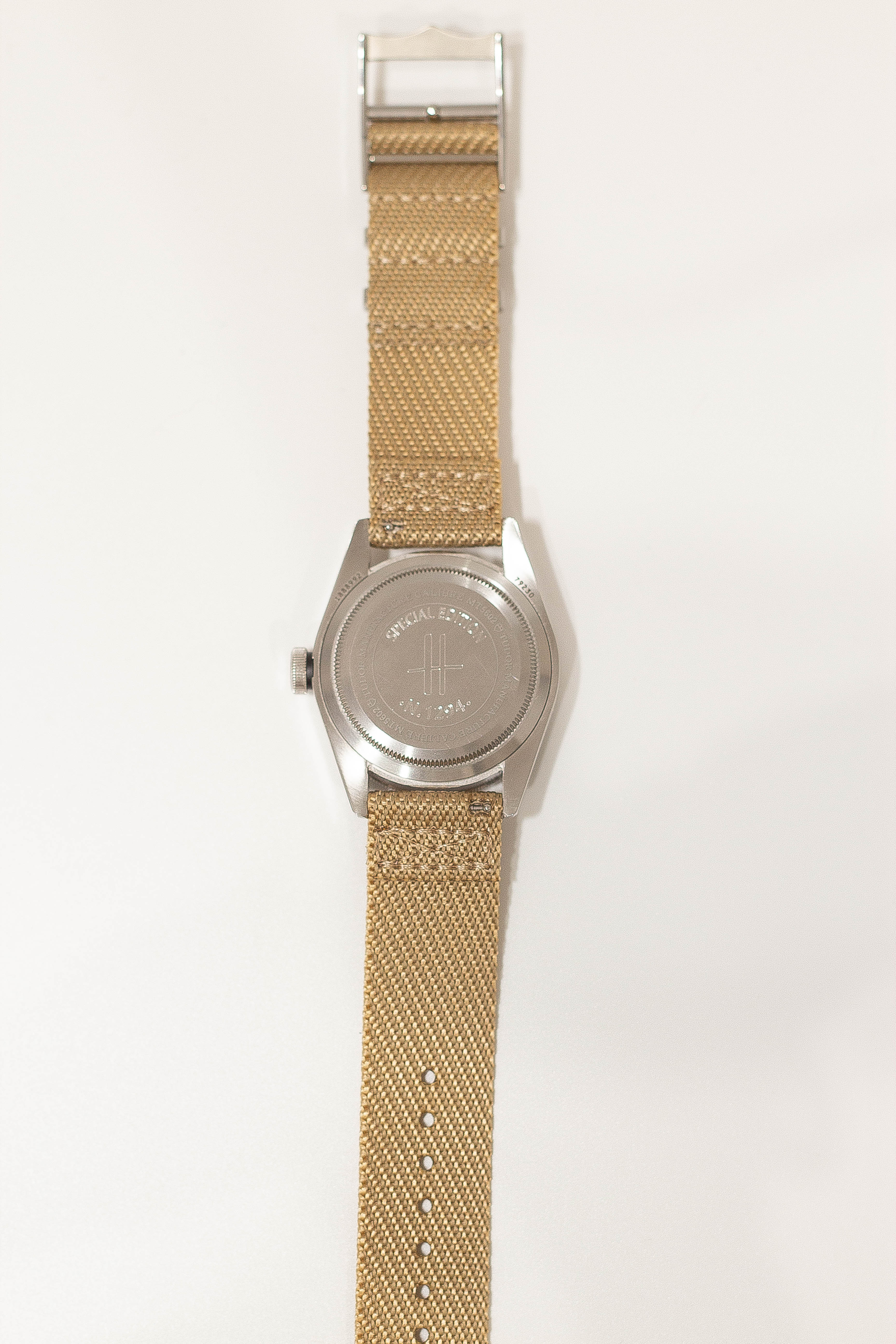 Stainless steel watch with tan canvas fabric strap and military-inspired cross emblem on dial