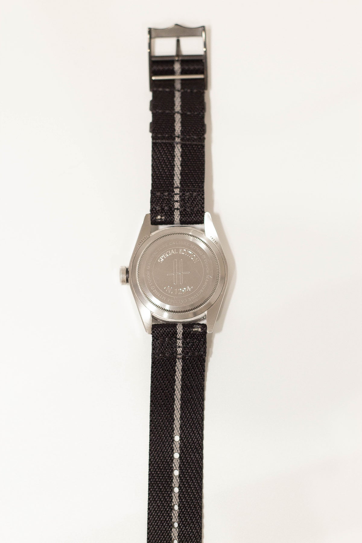 Stainless steel military watch with black and white striped fabric strap and engraved caseback
