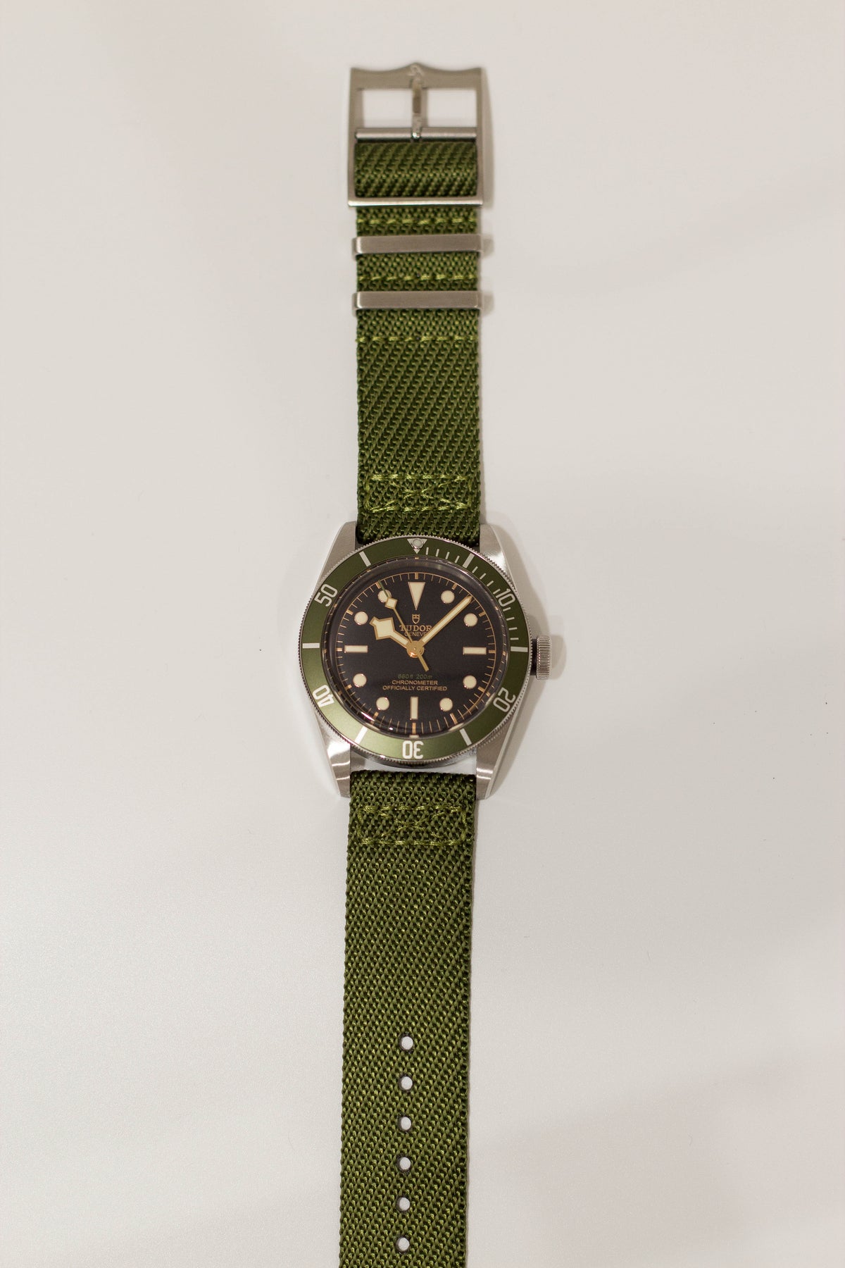 Vintage stainless steel dive watch with black dial, green bezel, applied indices, and olive green fabric strap with metal buckle