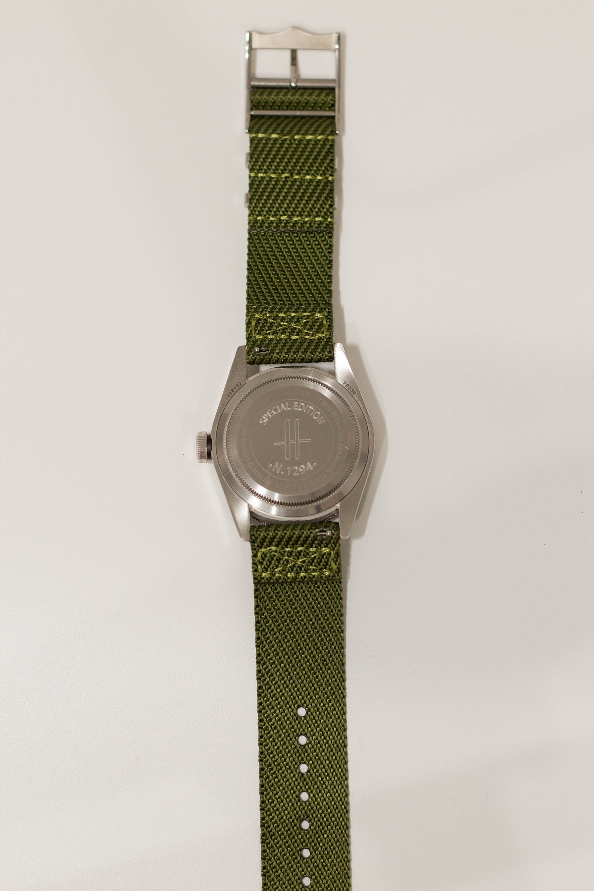 Military-style green canvas watch strap with stainless steel buckle and engraved caseback, compatible with smartwatch bands