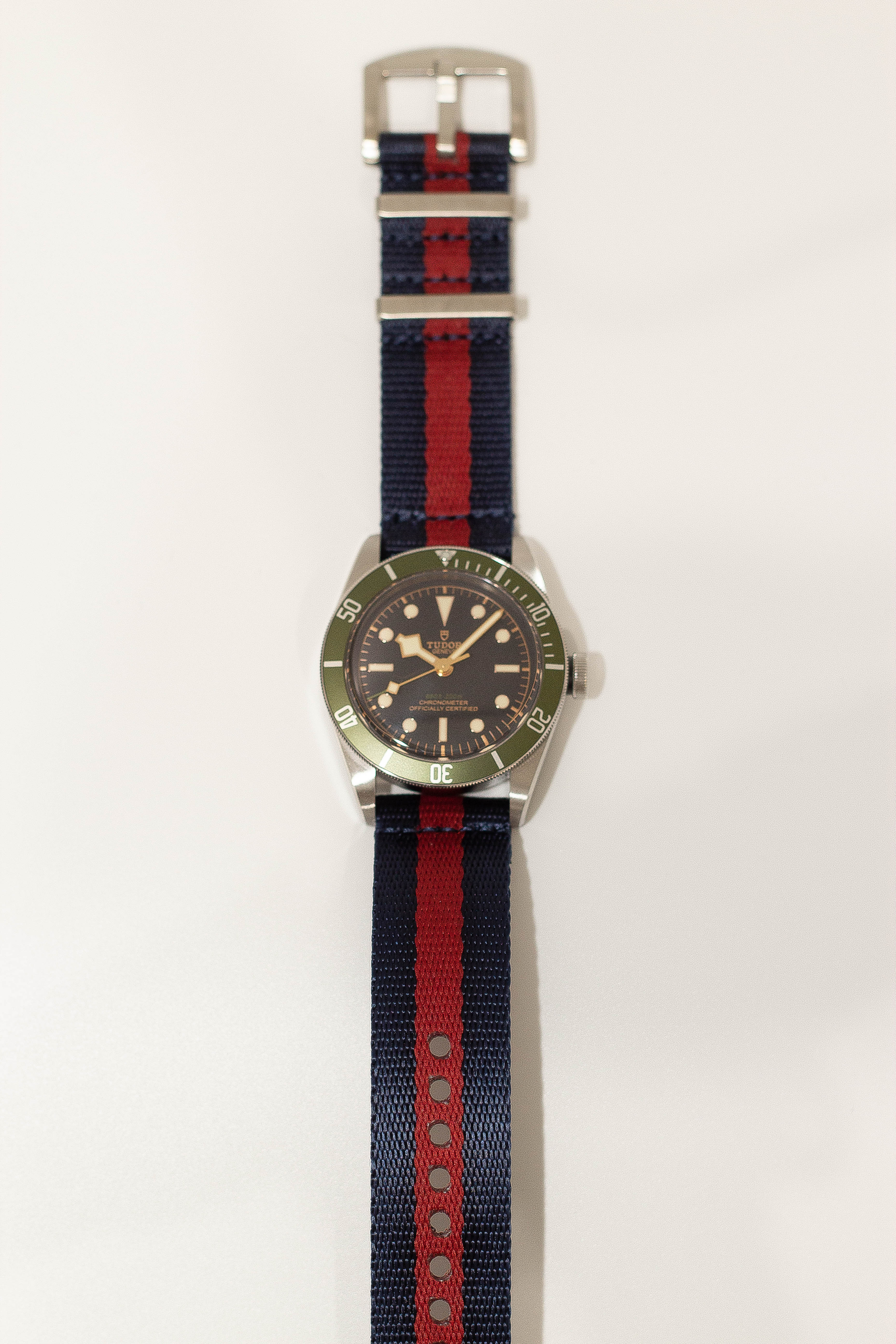 Vintage dive watch with olive green bezel, black dial, and steel case on navy blue and red striped fabric strap