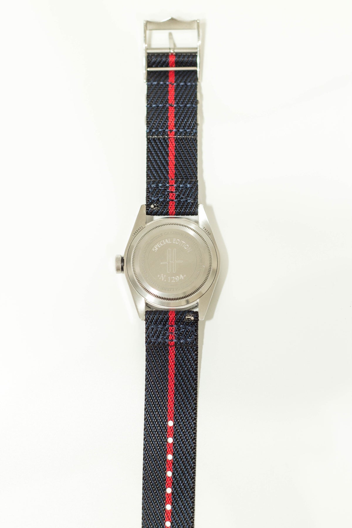 Stainless steel watch with black fabric band featuring red stripe and white dot details, silver case back engraved with special edition marking
