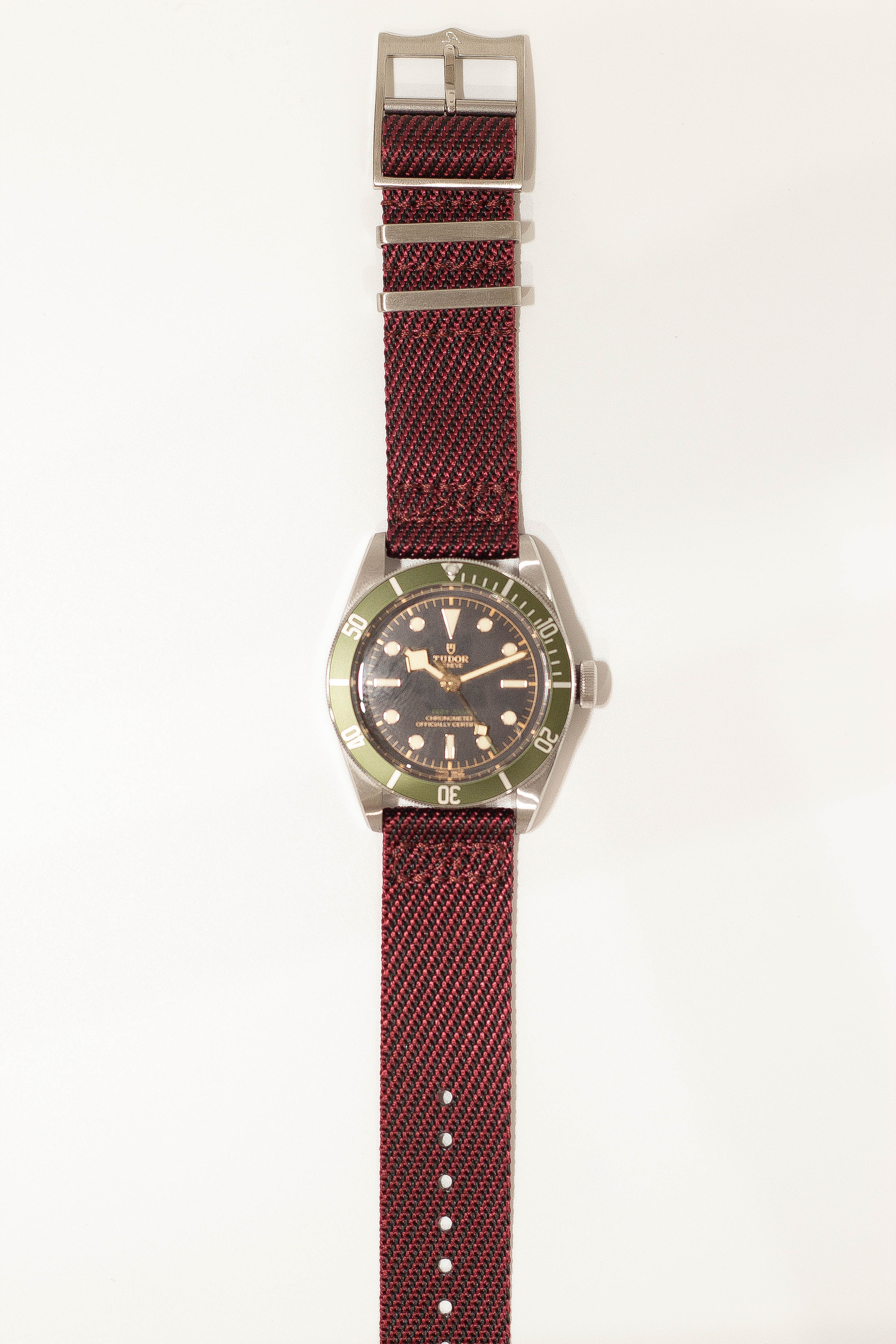 Tudor vintage dive watch with green bezel, black dial, and red fabric strap with metal buckle
