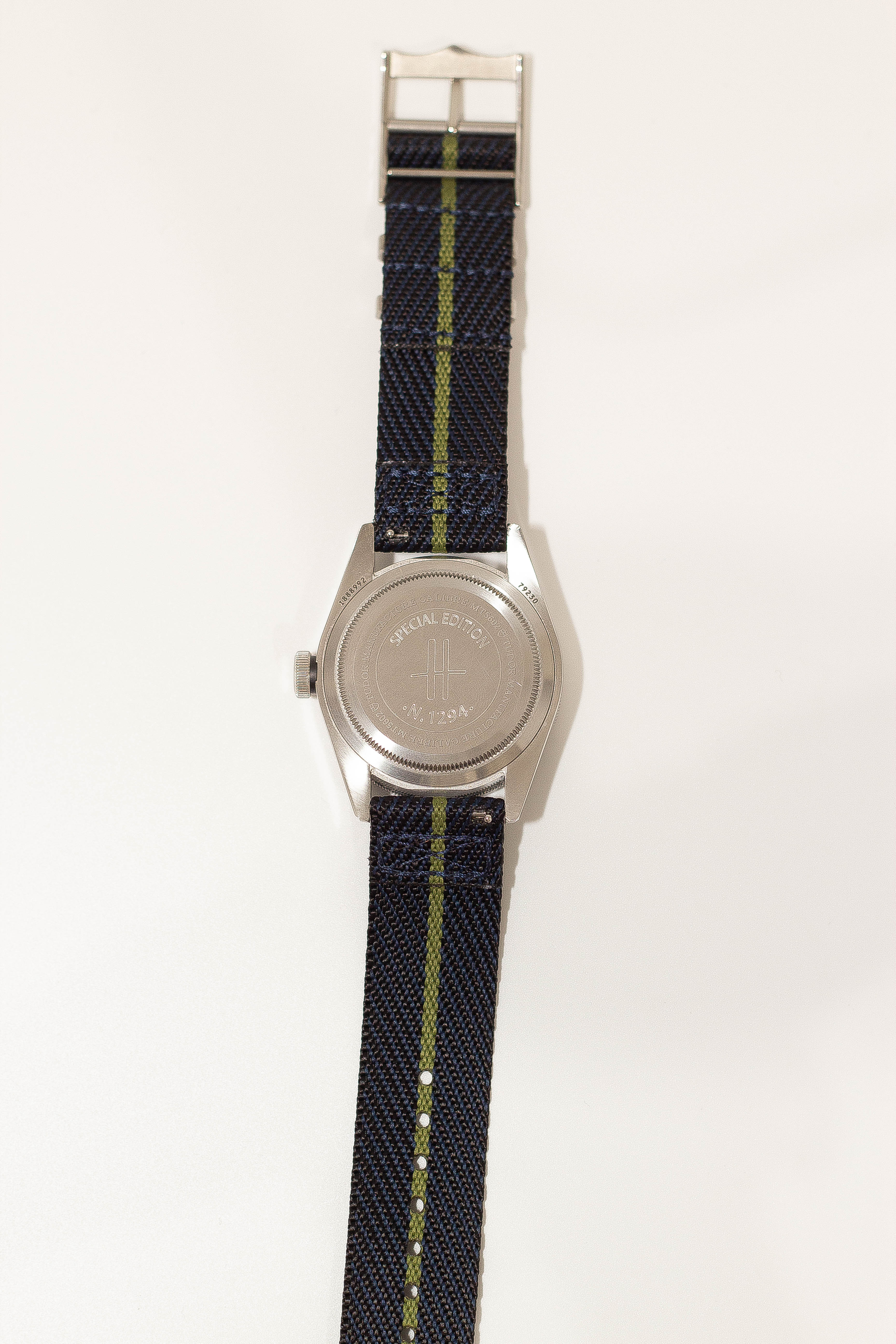 Military-style watch with stainless steel case, dark blue fabric band with green stripe, and special edition engraved caseback