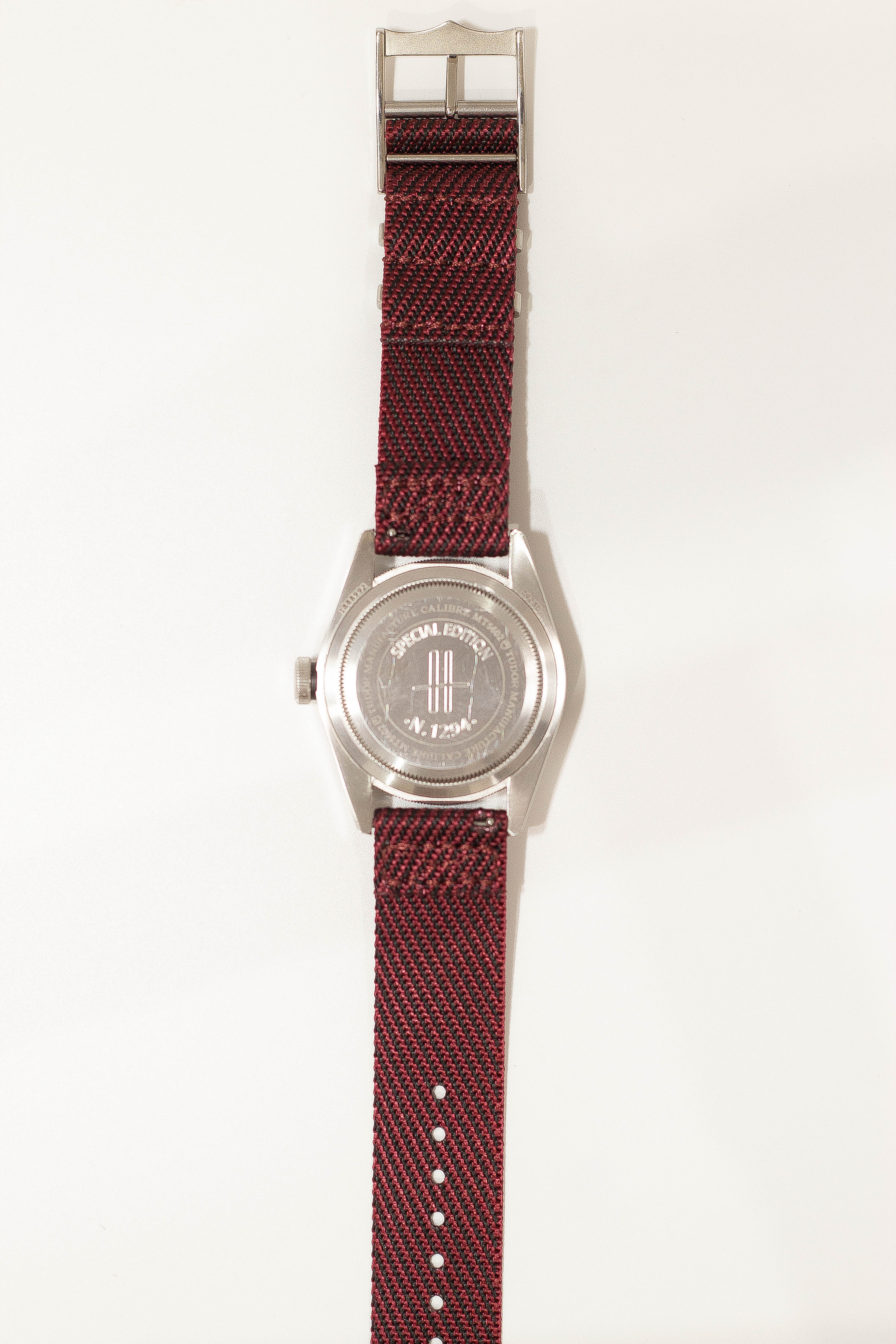 Silver-tone watch with red and black woven fabric strap and decorative buckle closure displayed flat