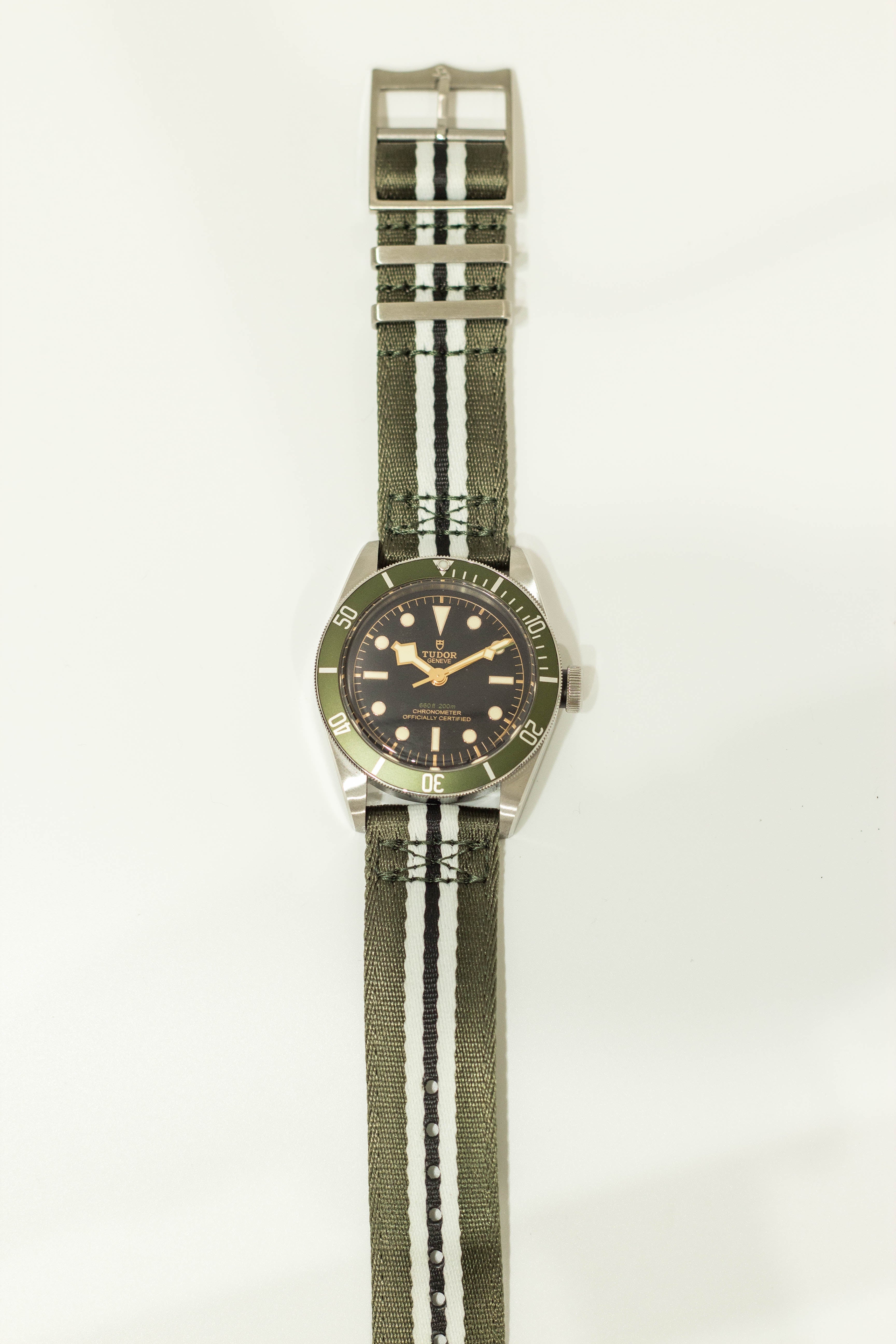 Tudor Black Bay dive watch with green bezel, black dial, gold hands, and green striped military fabric strap