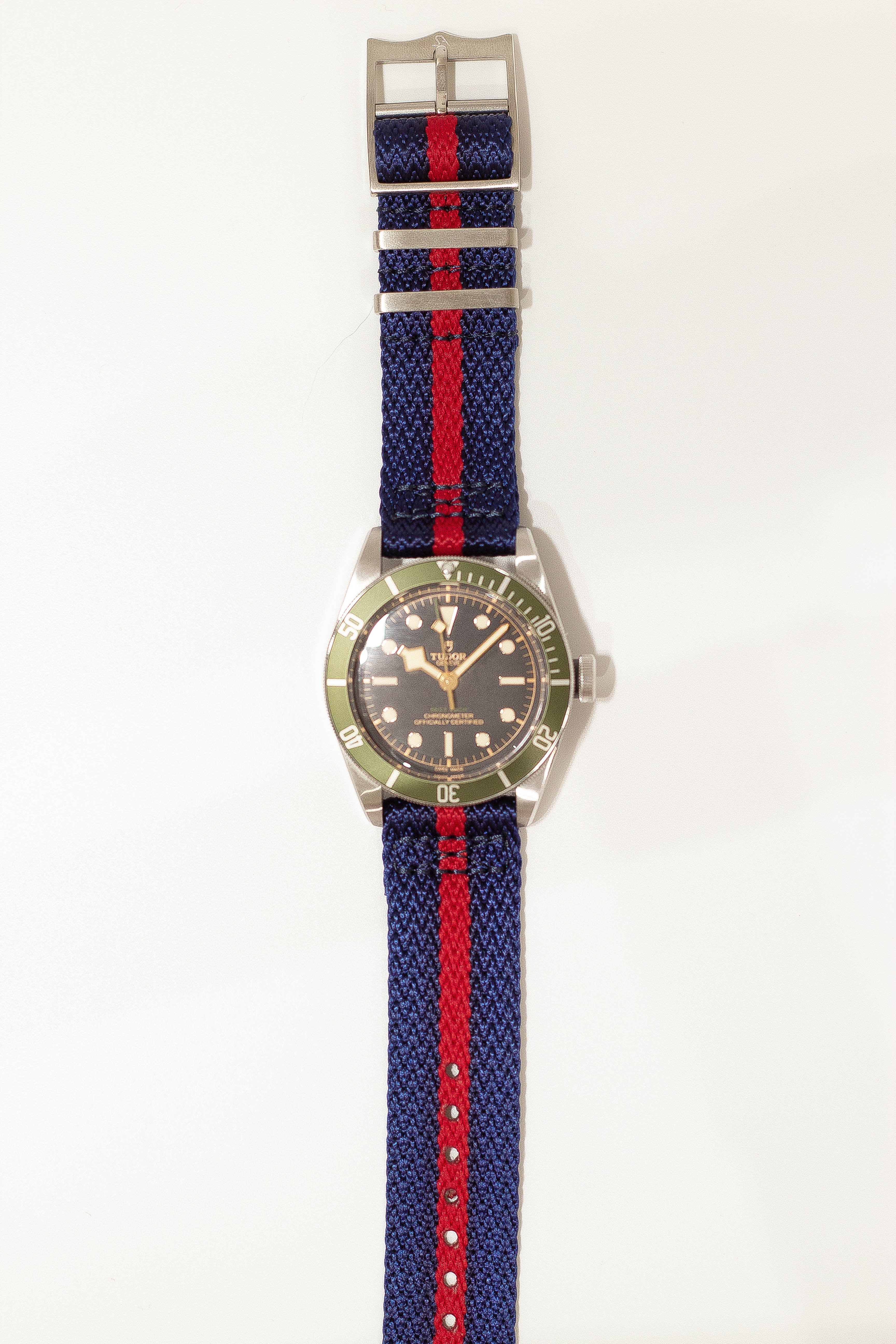 Tudor Black Bay dive watch with green bezel and navy red striped fabric strap