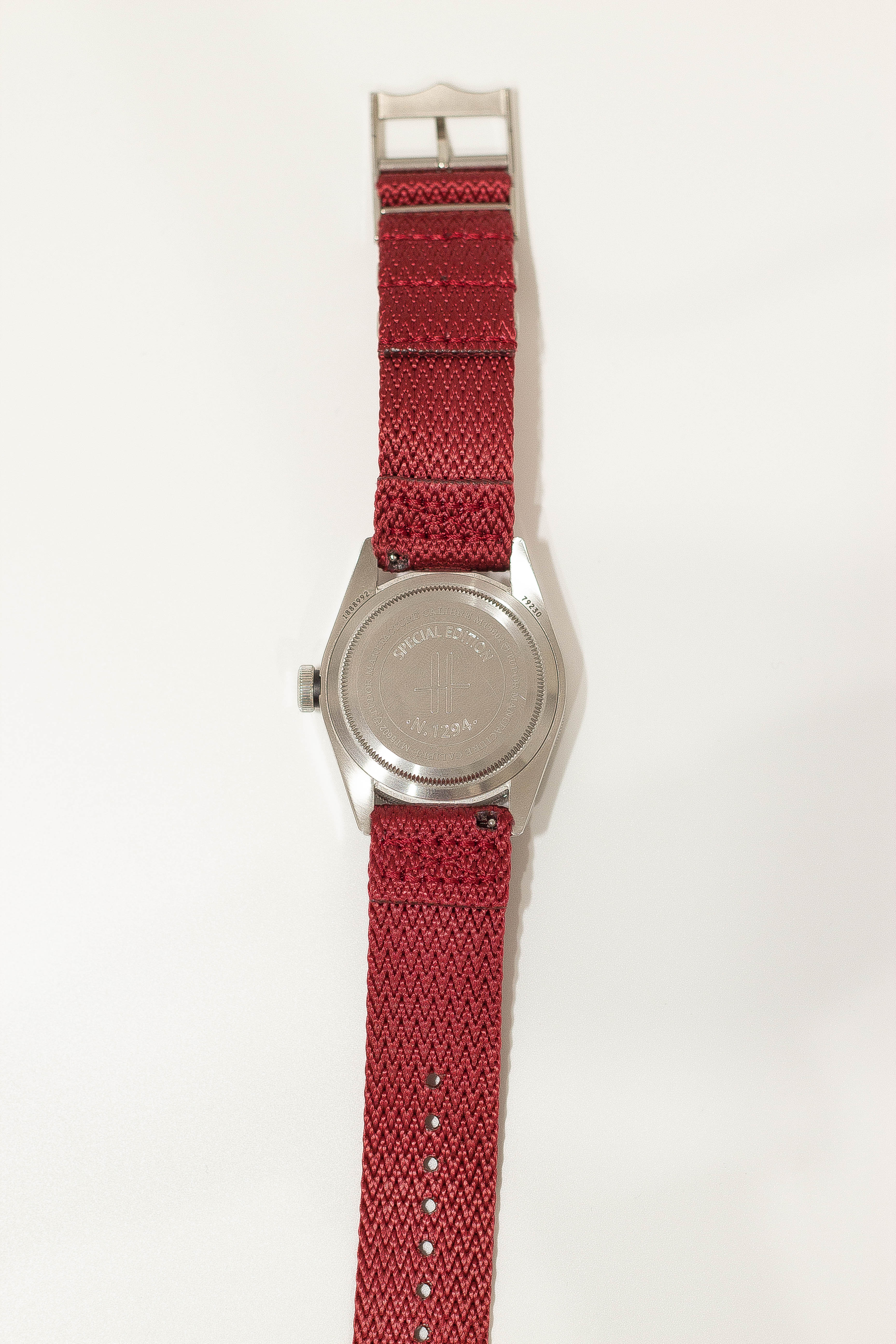 Silver military watch with red fabric strap and decorative striped trim detail