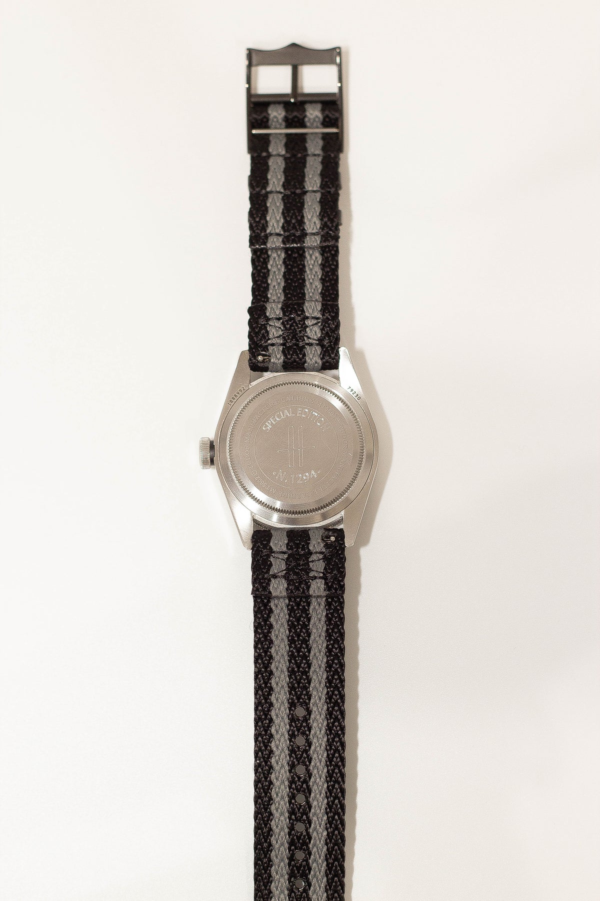 Stainless steel watch with black and grey striped fabric strap and metal hardware clasp