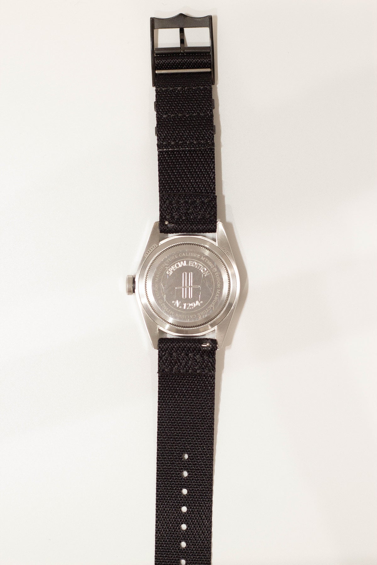 Military canvas watch strap with black hardware, stainless steel buckle and engraved caseback on white background