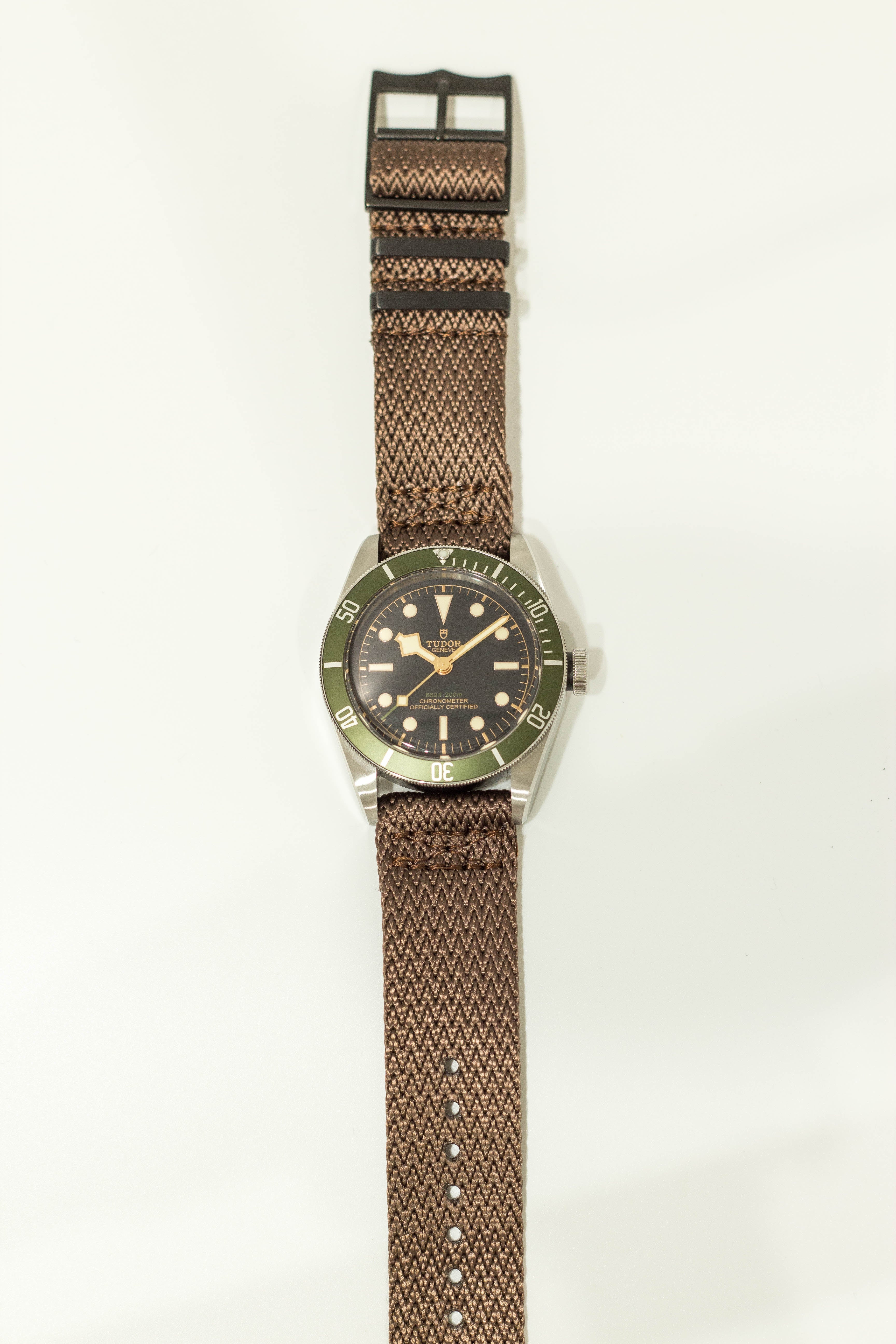 Vintage dive watch with green bezel, black dial, cream numerals, and brown fabric quick-release strap with black hardware