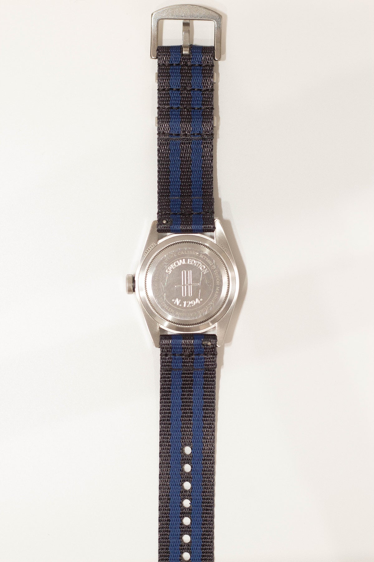 Stainless steel watch with dark blue and charcoal woven military-style fabric strap and engraved case back