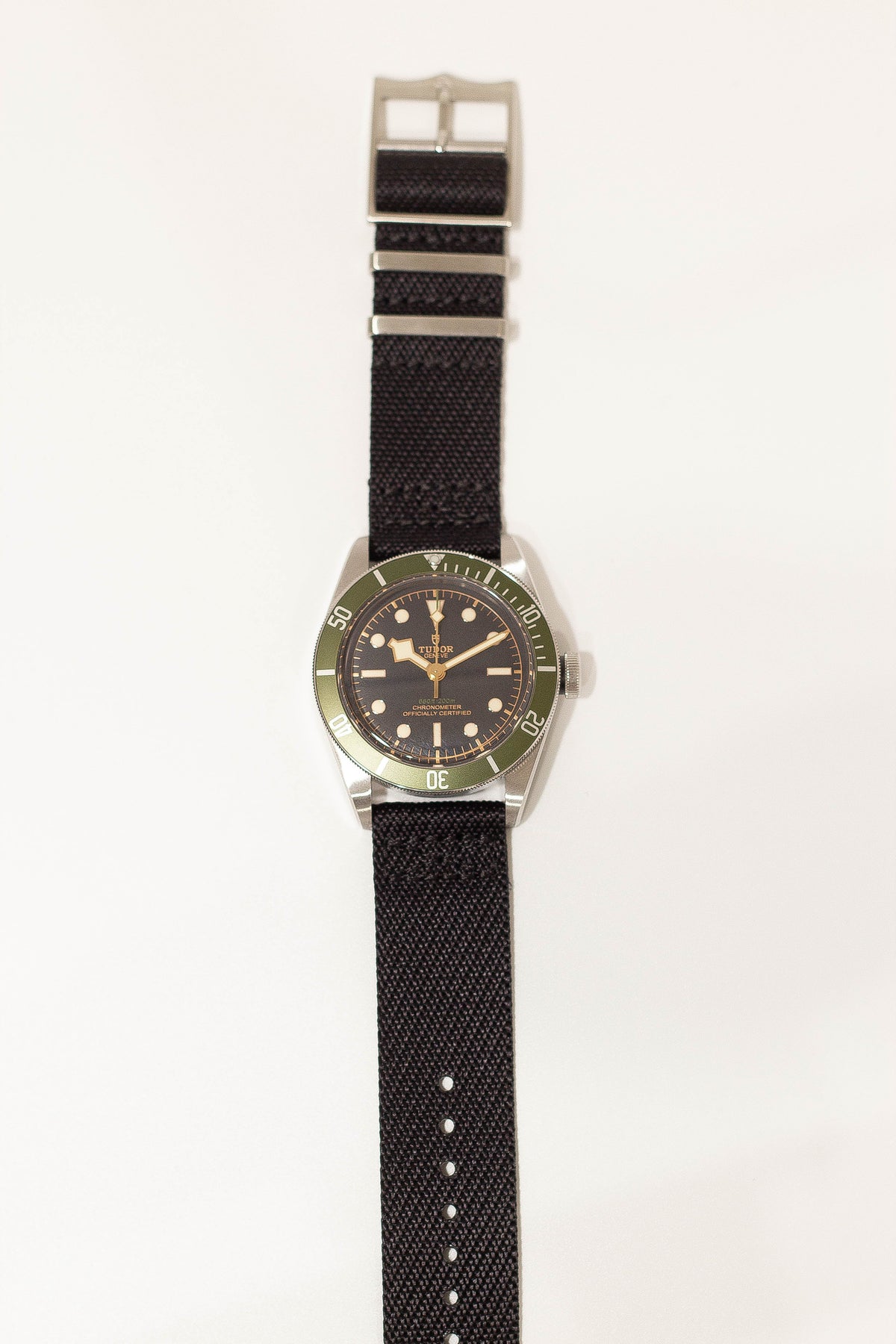 Tudor Black Bay dive watch with steel case, green bezel, black dial, and black fabric strap with hardware