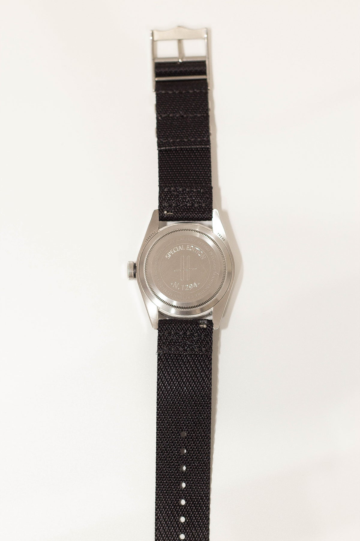 Stainless steel watch with black fabric strap and special edition case back design, displayed flat against white background