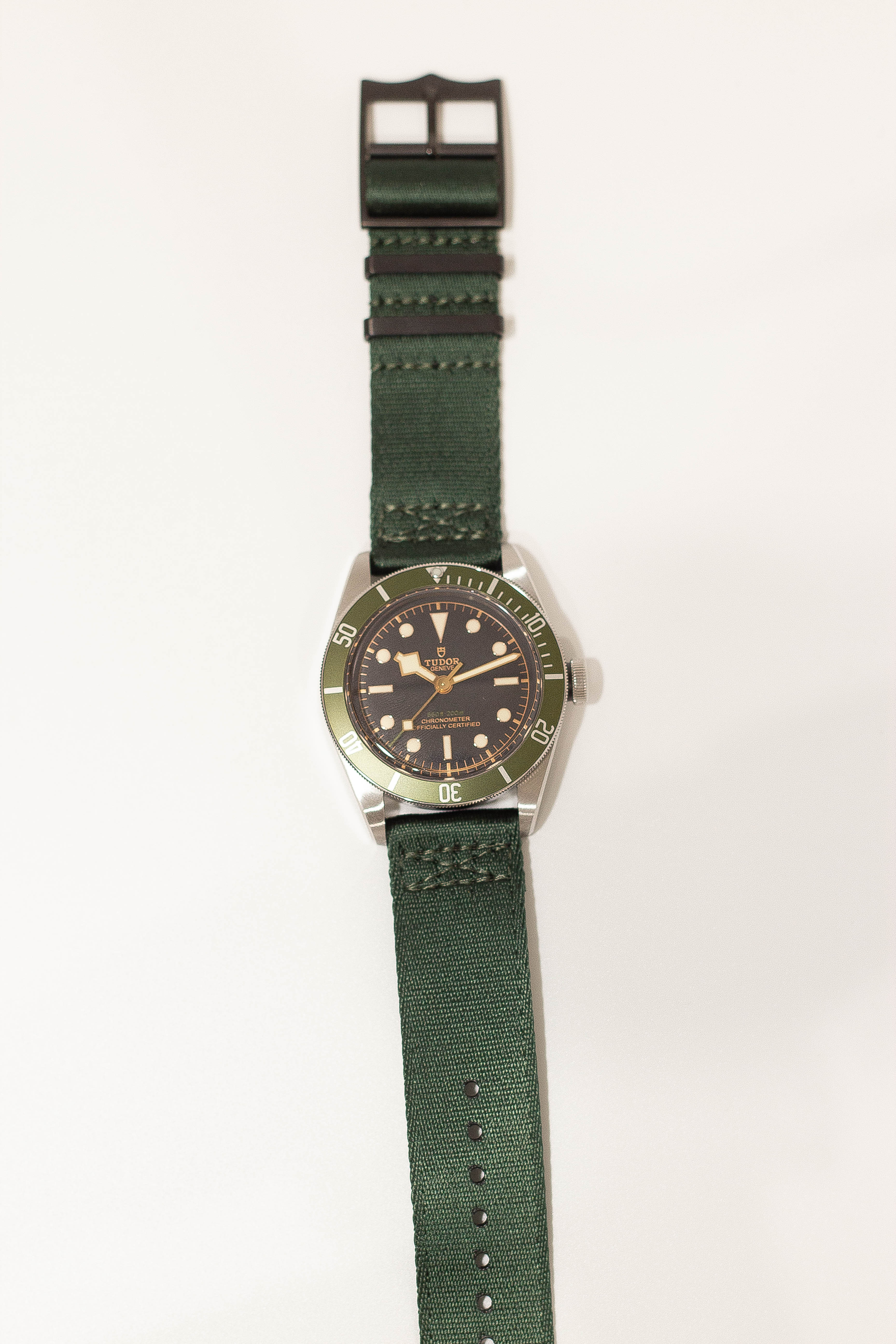 Vintage Tudor dive watch with black dial, green rotating bezel, and stainless steel case on green canvas NATO-style strap