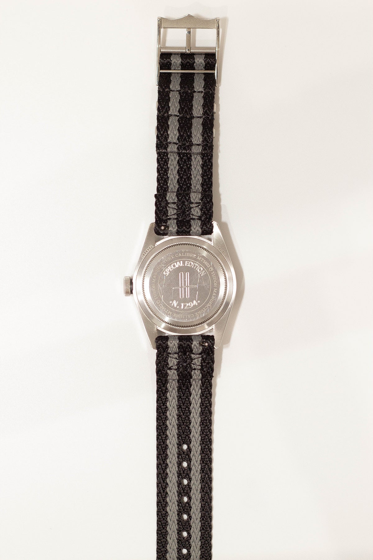 Silver watch with black and grey striped fabric strap and special edition dial on white background