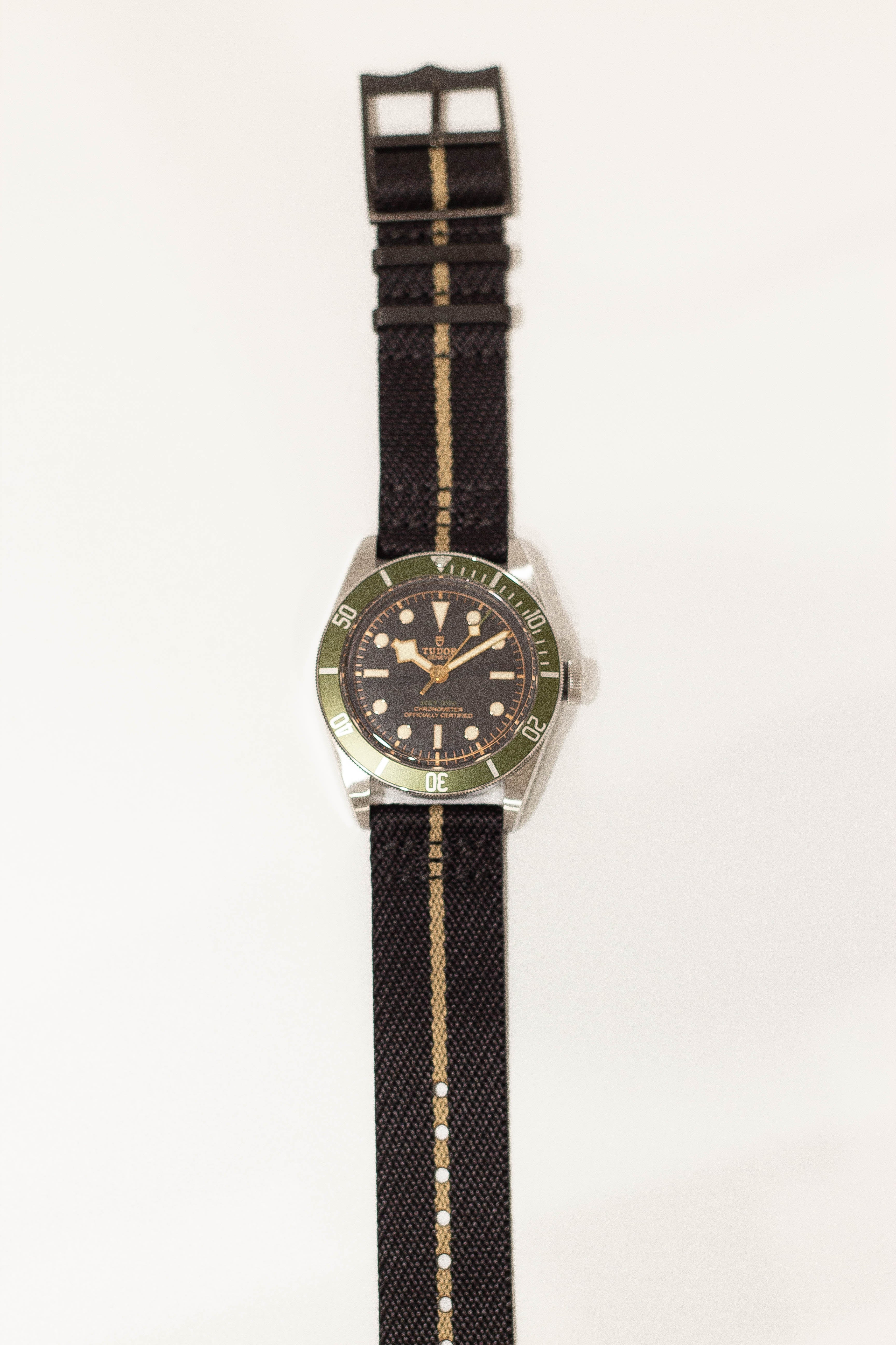 Dive watch with green bezel on black fabric strap with wheat stripe