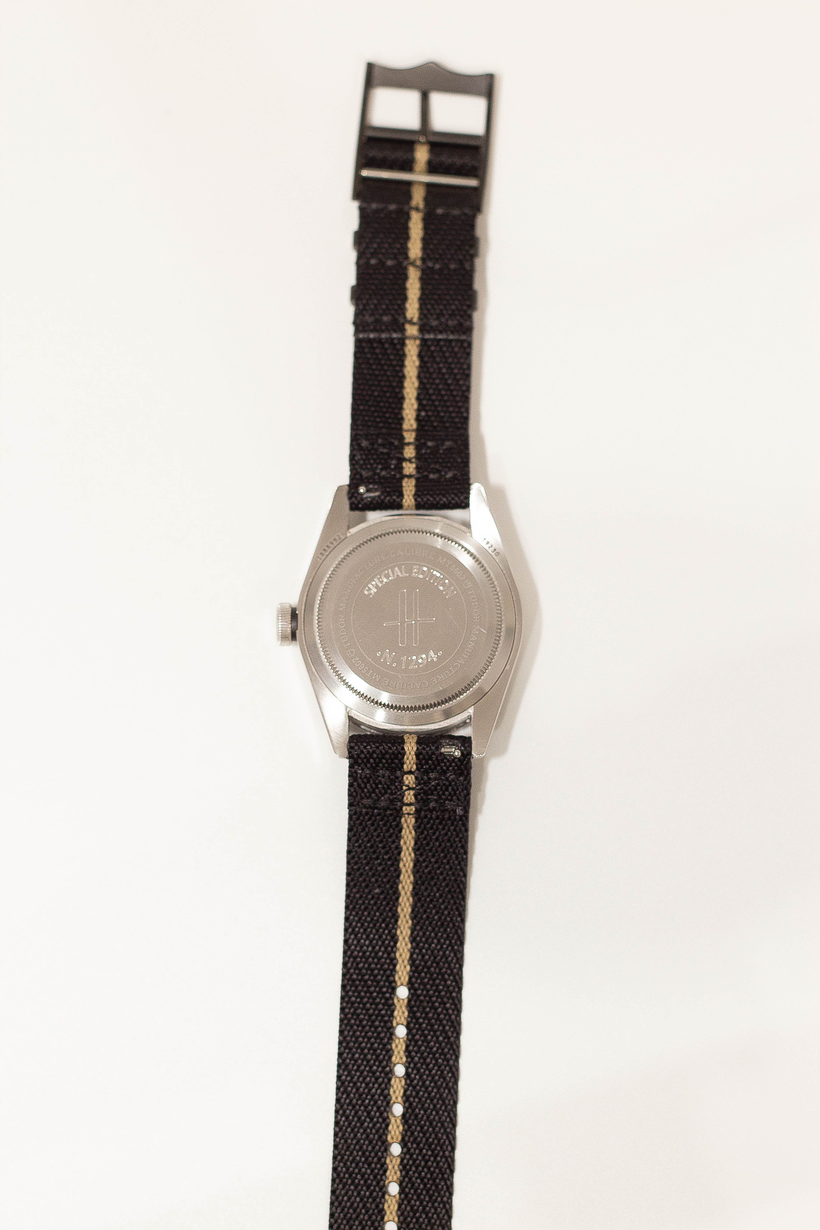 Military watch with silver case, black fabric strap with tan stripe, and special forces dial