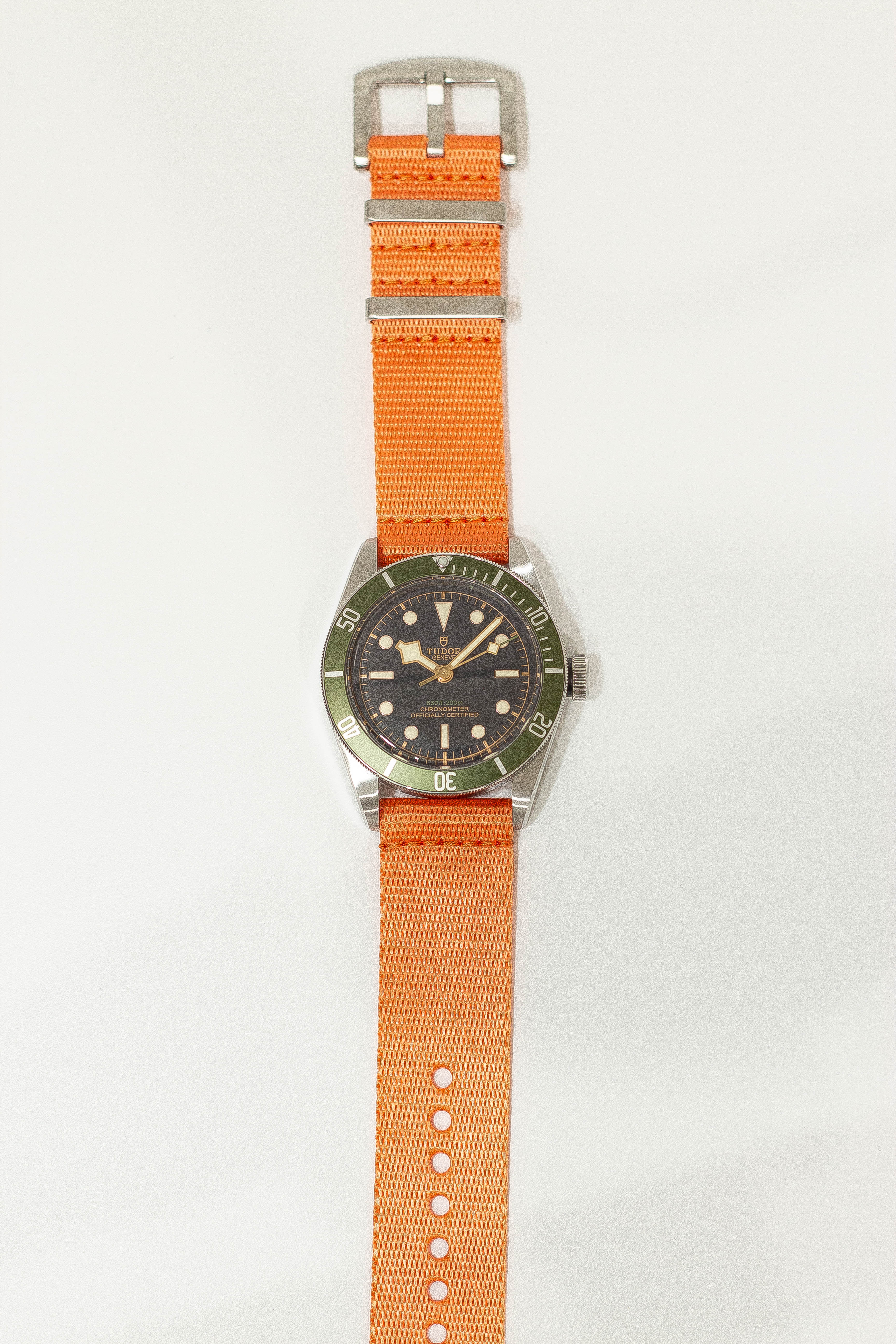 Vintage-style dive watch with black dial, green bezel, silver case, and orange fabric military strap with buckle