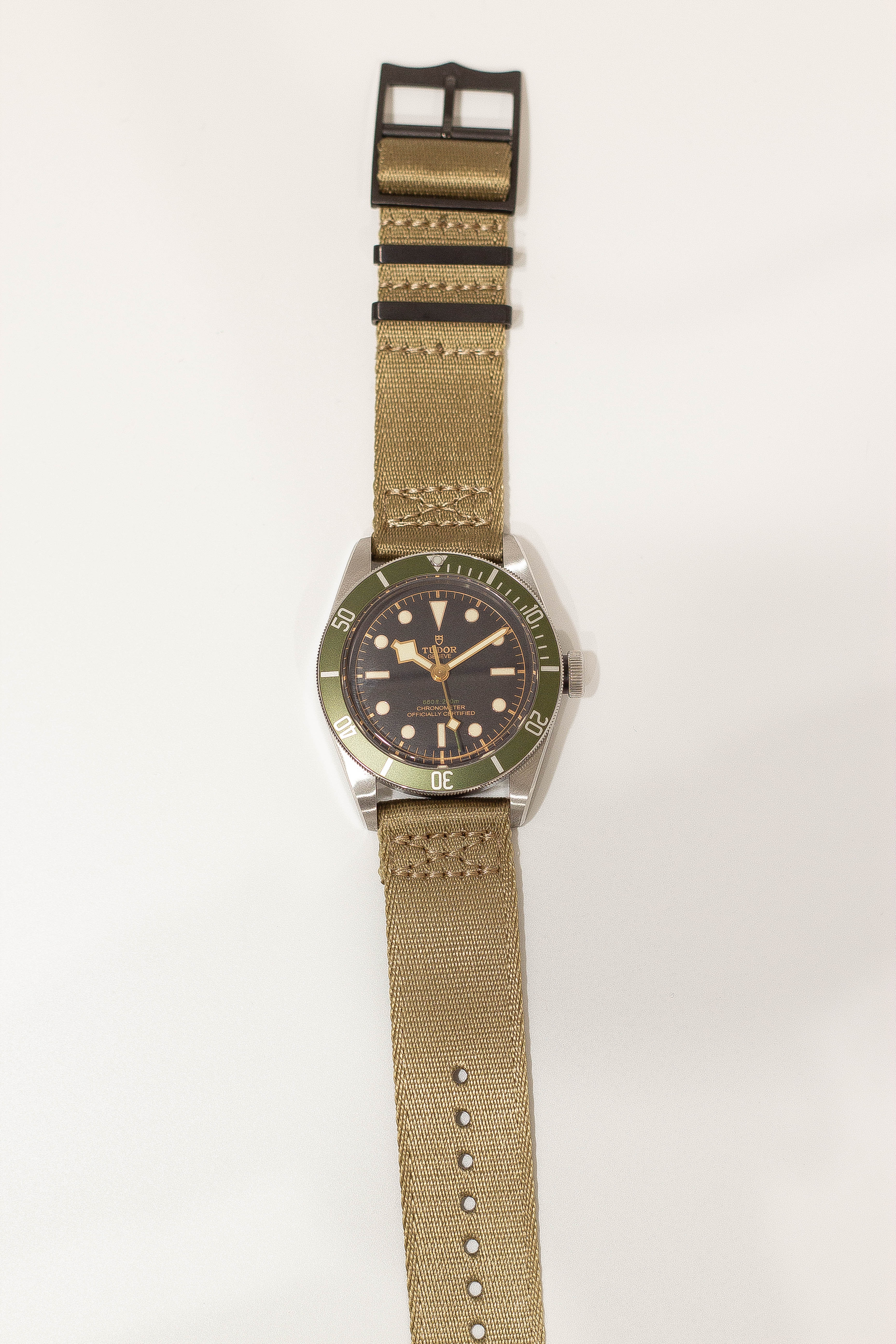 Tudor Black Bay vintage-style dive watch with green bezel, black dial, stainless steel case and tan canvas military strap