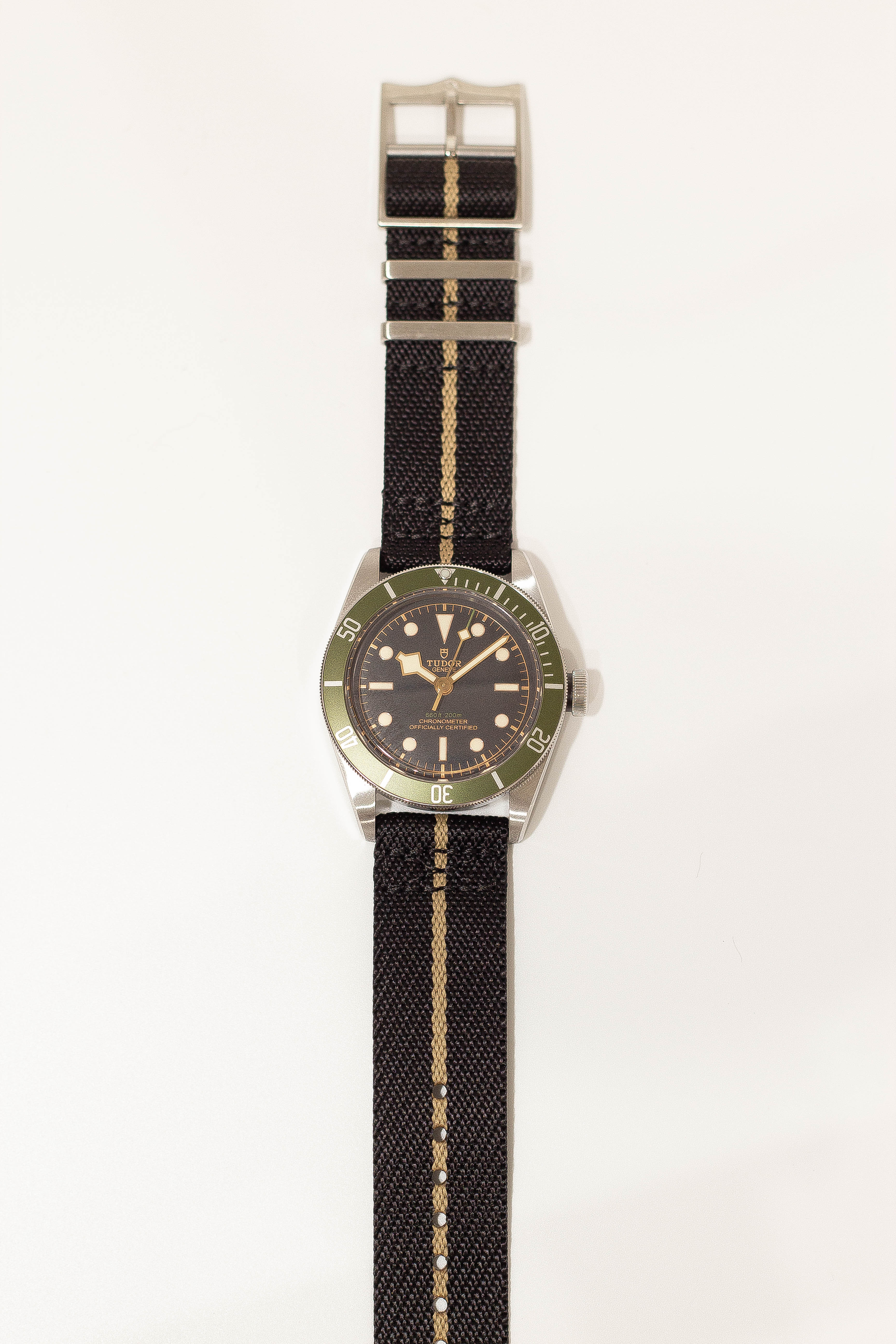 Vintage Tudor dive watch with green bezel, black dial, stainless steel case and black fabric strap with tan stripe