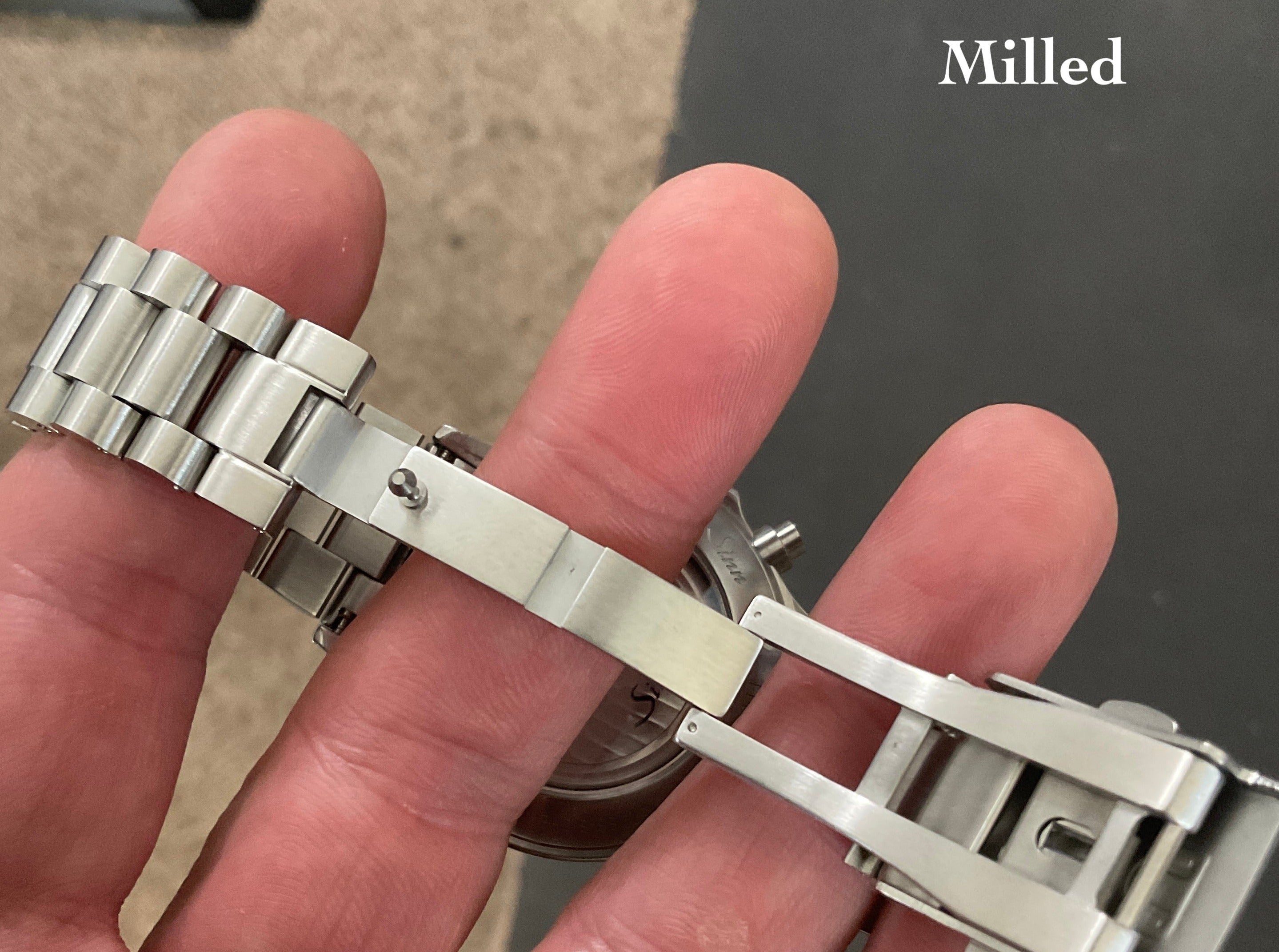 Polished stainless steel watch bracelet with milled end links displayed on hand, showing chain links detail