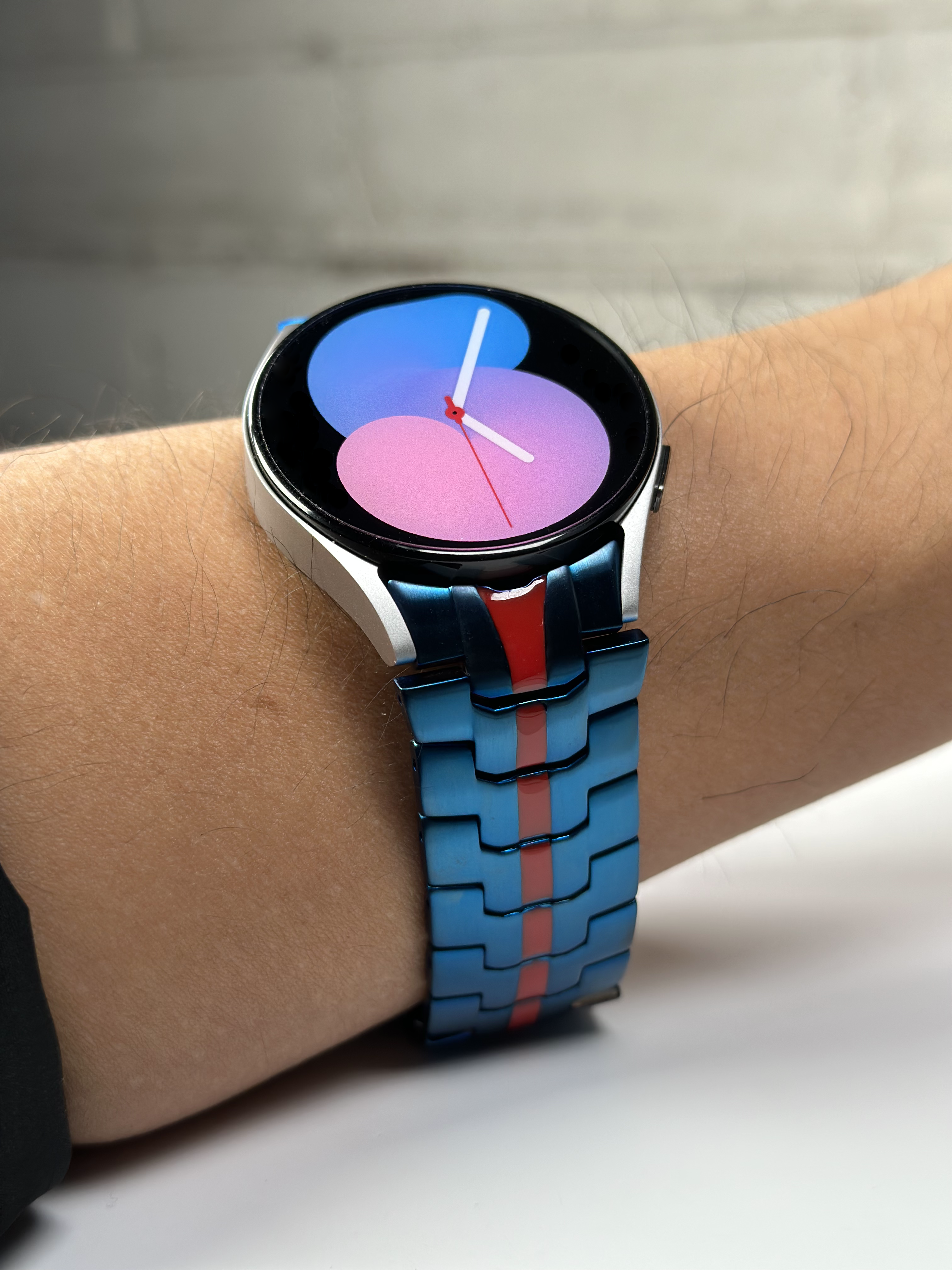 Modern smartwatch with blue and red steel bracelet displayed on wrist, featuring colorful gradient watch face