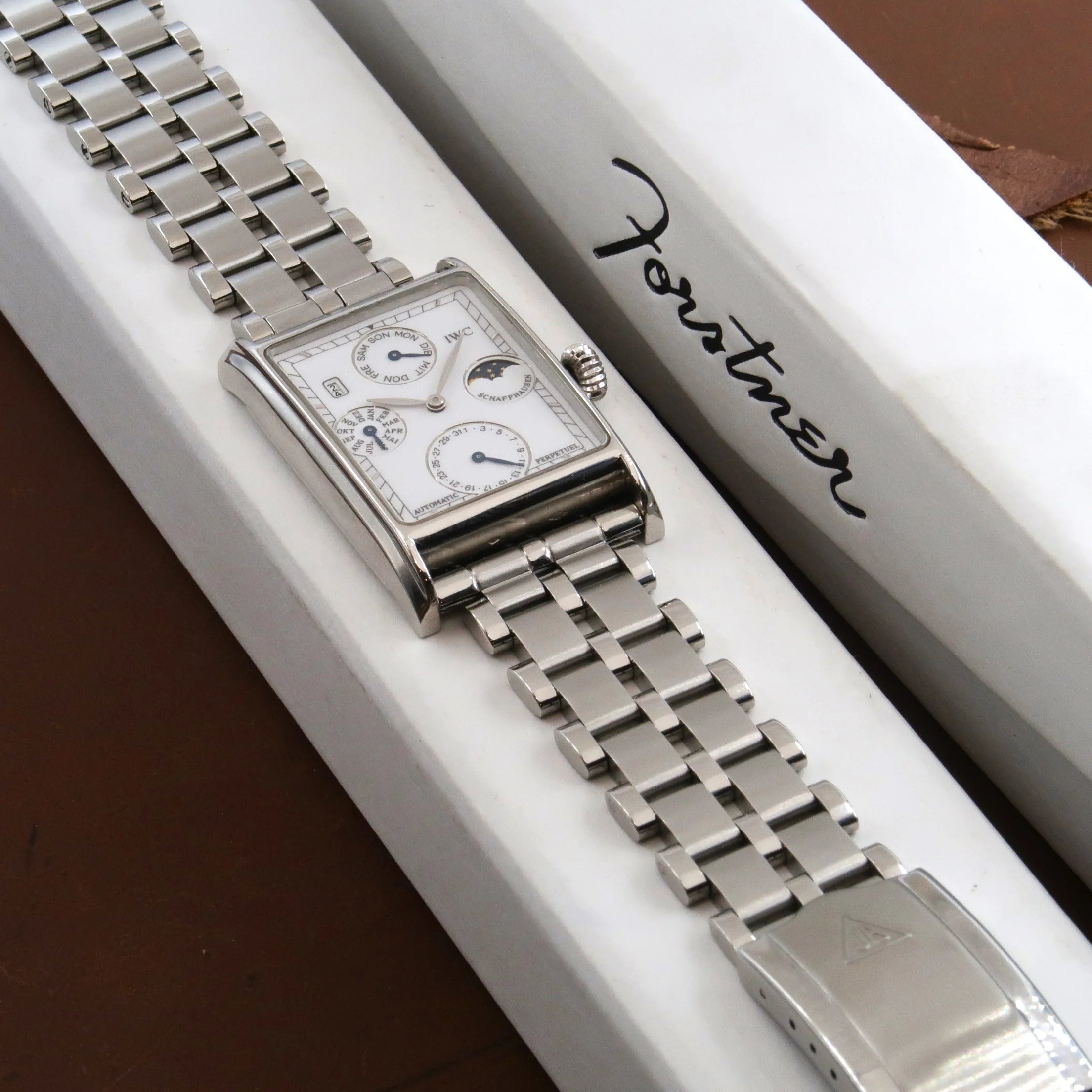 IWC stainless steel rectangular watch with moon phase complications and integrated five-row bracelet on white display pillow