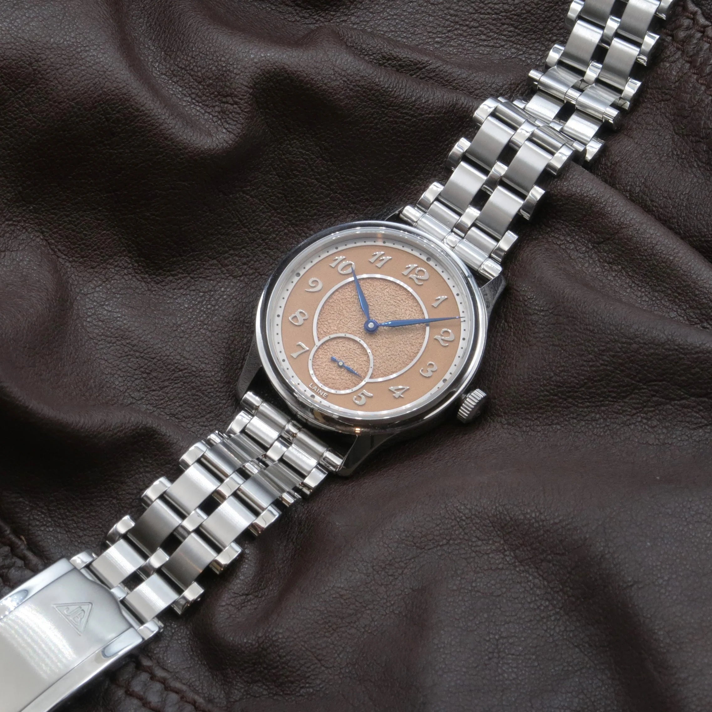 Stainless steel watch with beige dial and sub-dial, 5-row beads of rice bracelet, displayed on dark leather background