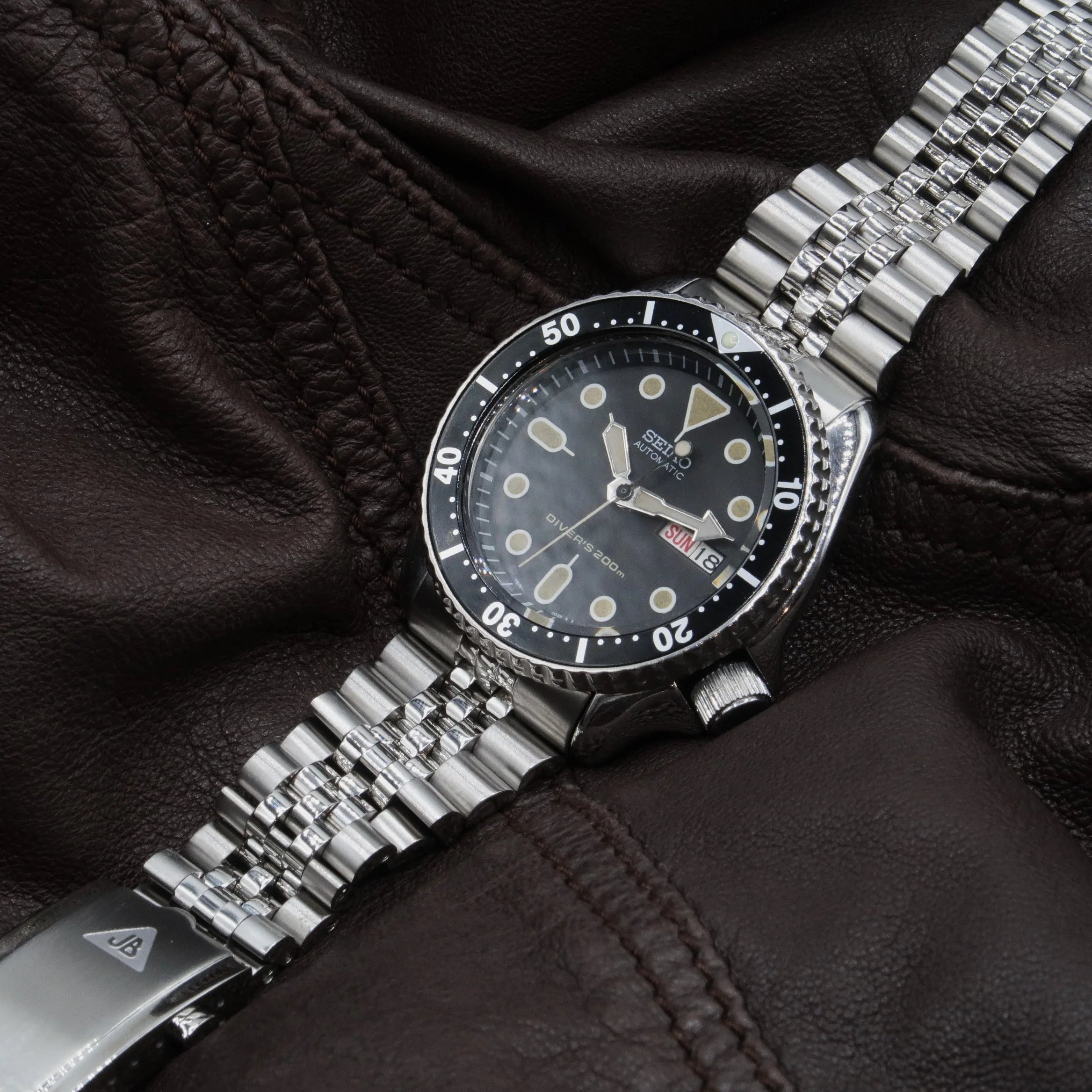 Seiko SKX automatic diving watch with black dial, stainless steel bracelet and bezel on leather background