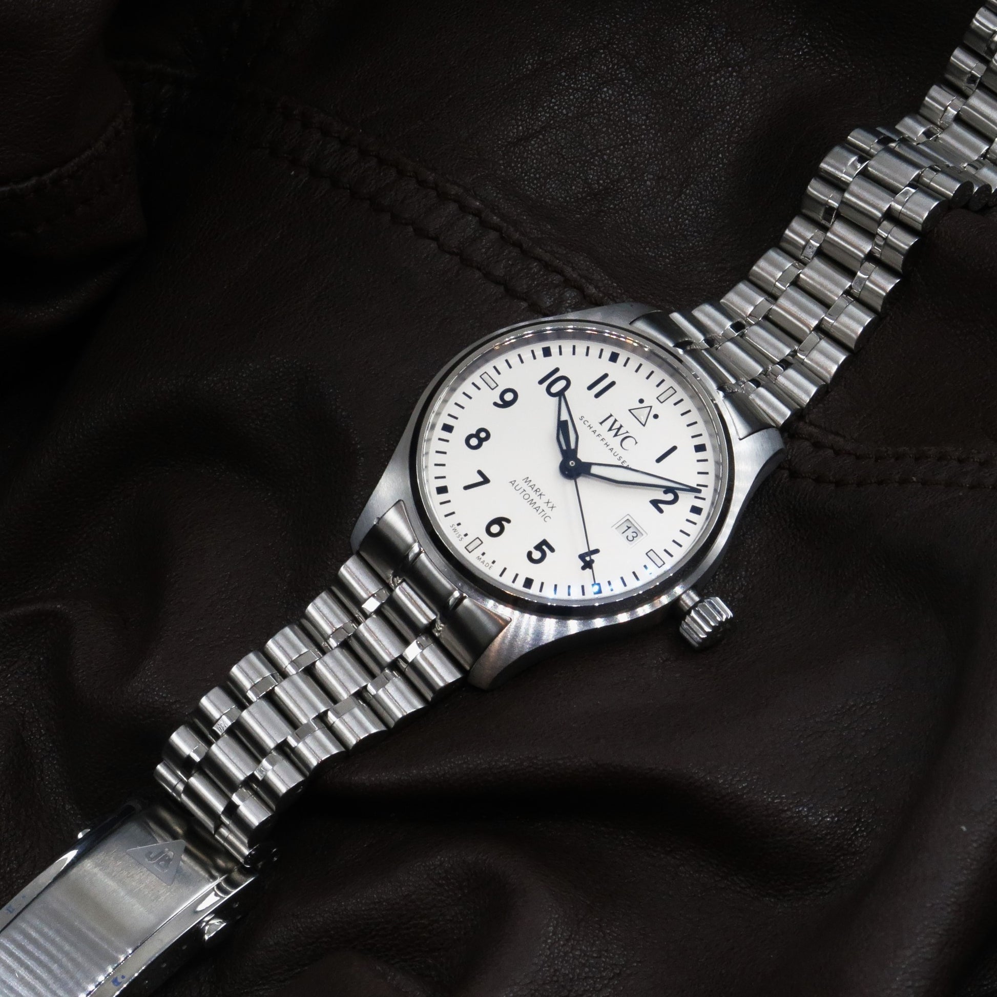 IWC Mark XX stainless steel pilot watch with white dial and integrated metal bracelet on black leather background