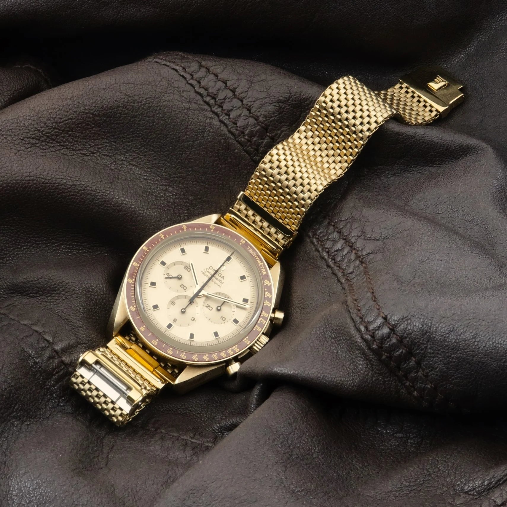 Gold plated mesh watch bracelet with straight ends on luxury chronograph timepiece against black leather background
